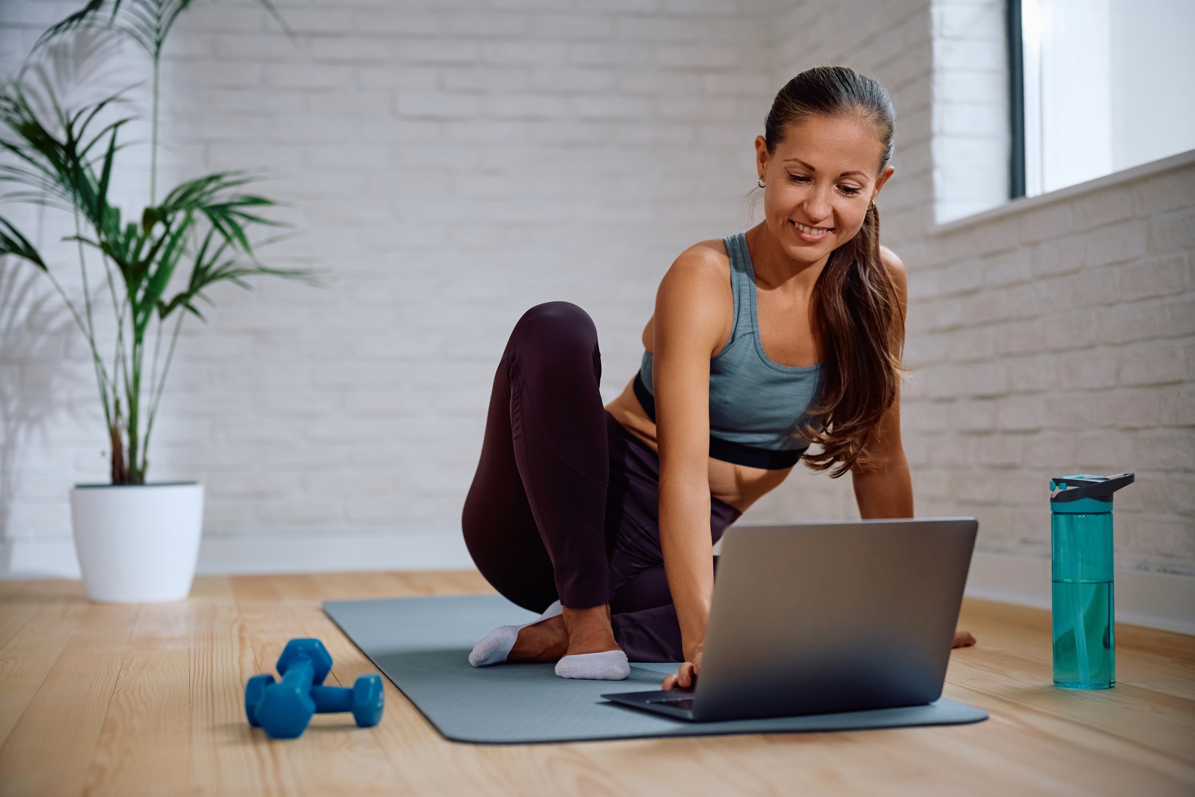 Happy athletic woman following online exercise class over laptop. Copy space.