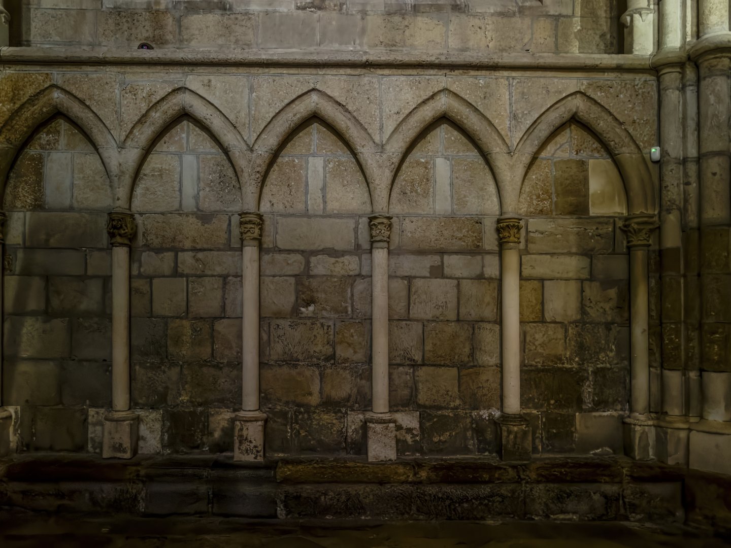 Medieval stone wall with pointed Gothic arches and columns in a cathedral arcade