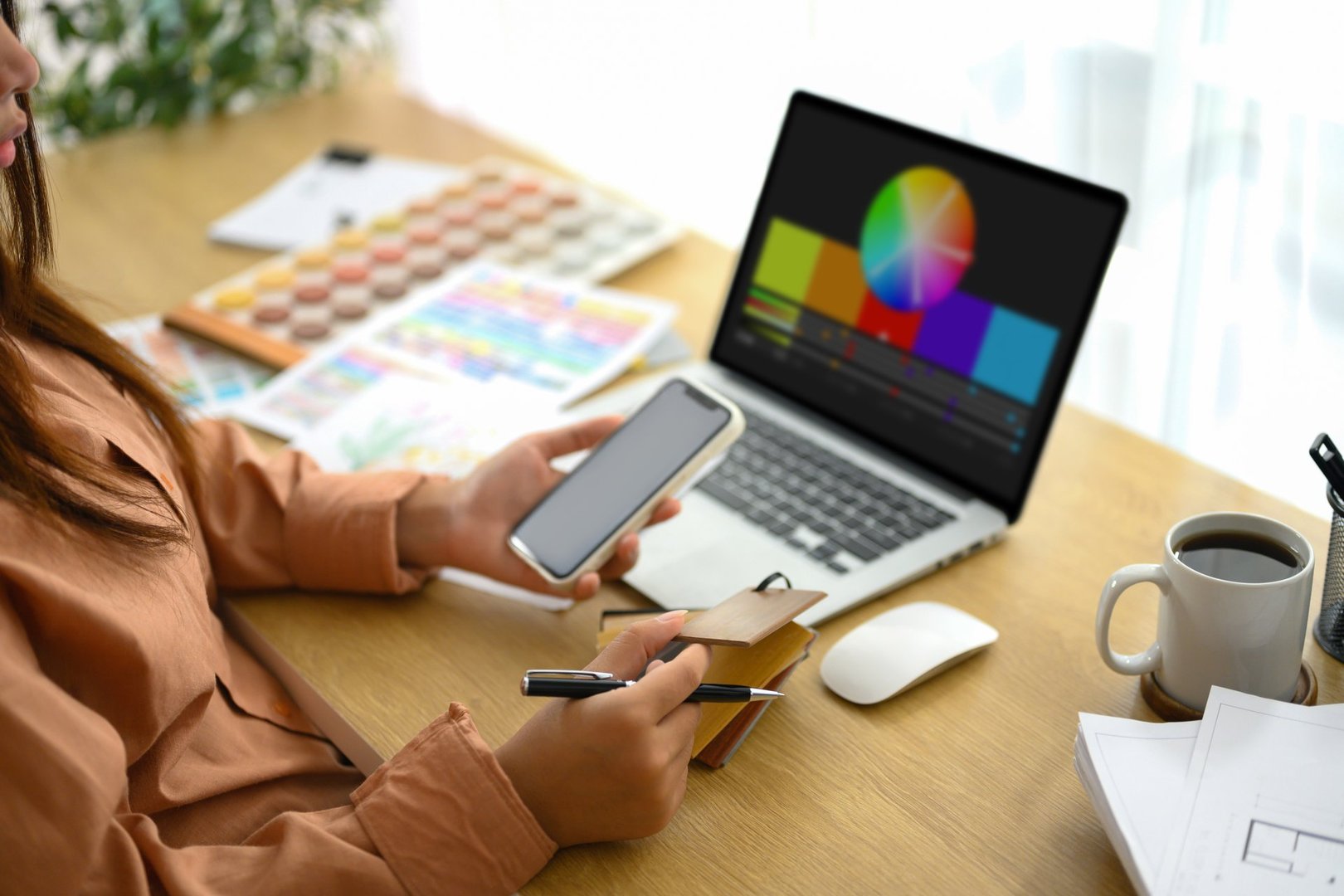 Female designer holding smartphone working with material and color samples at workplace.