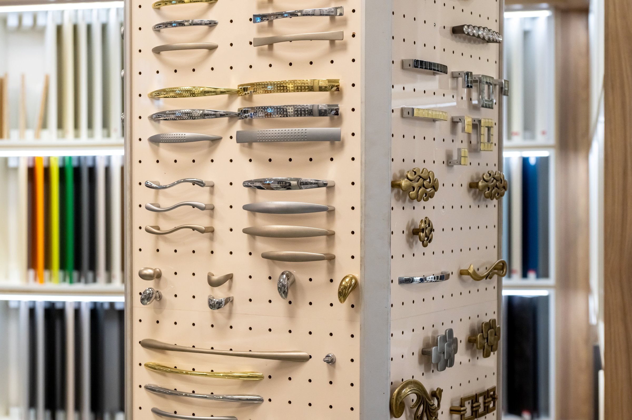 Display of assorted cabinet handles and knobs on pegboard. Interior design and hardware selection.