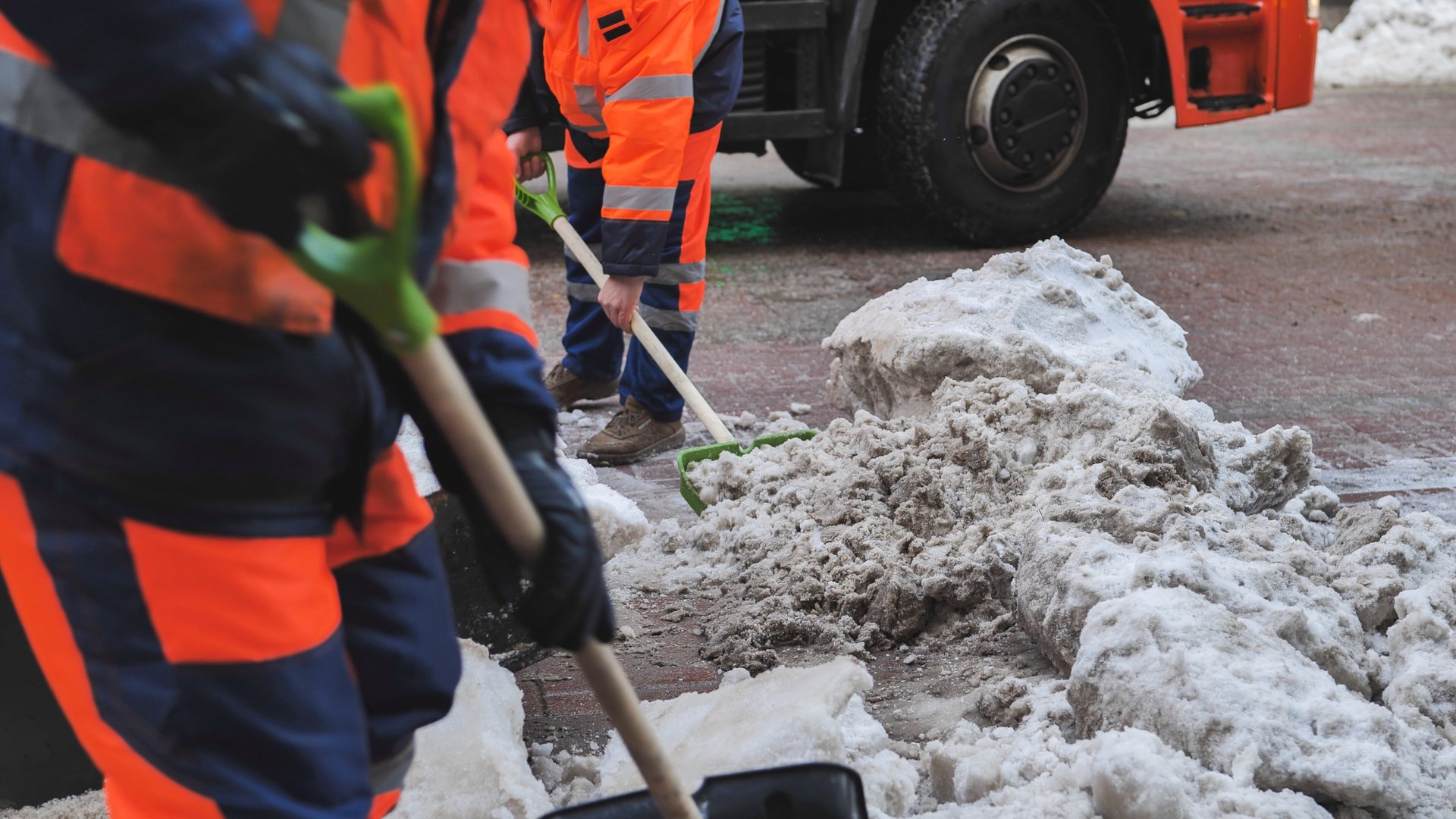 Road workers cleaning dirty snow from street after snowfall with shovels and truck