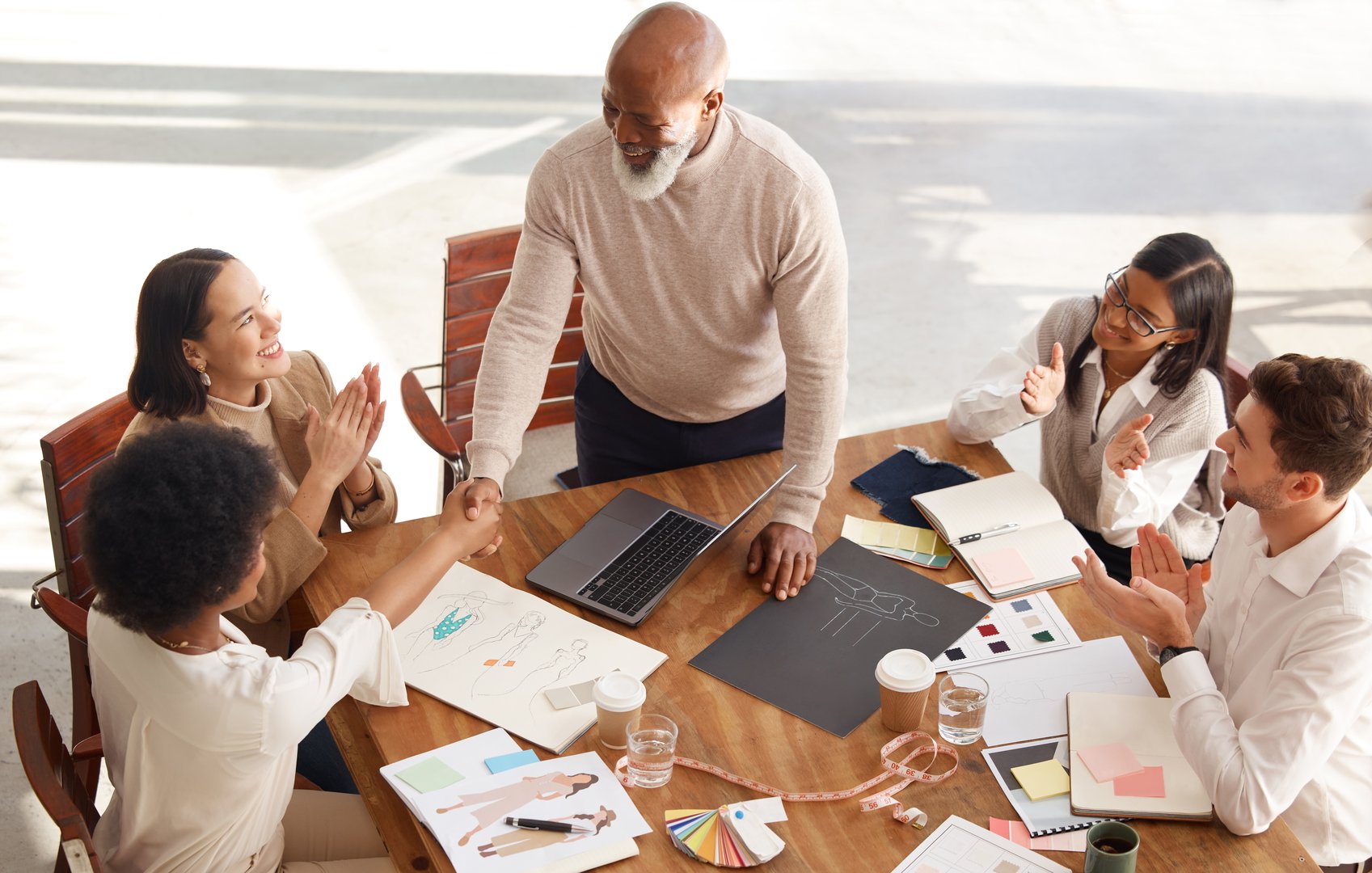Creative business people, meeting and handshake in planning above for fashion design, success or strategy at office. Senior clothing CEO man shaking hands with employee with team applause for startup