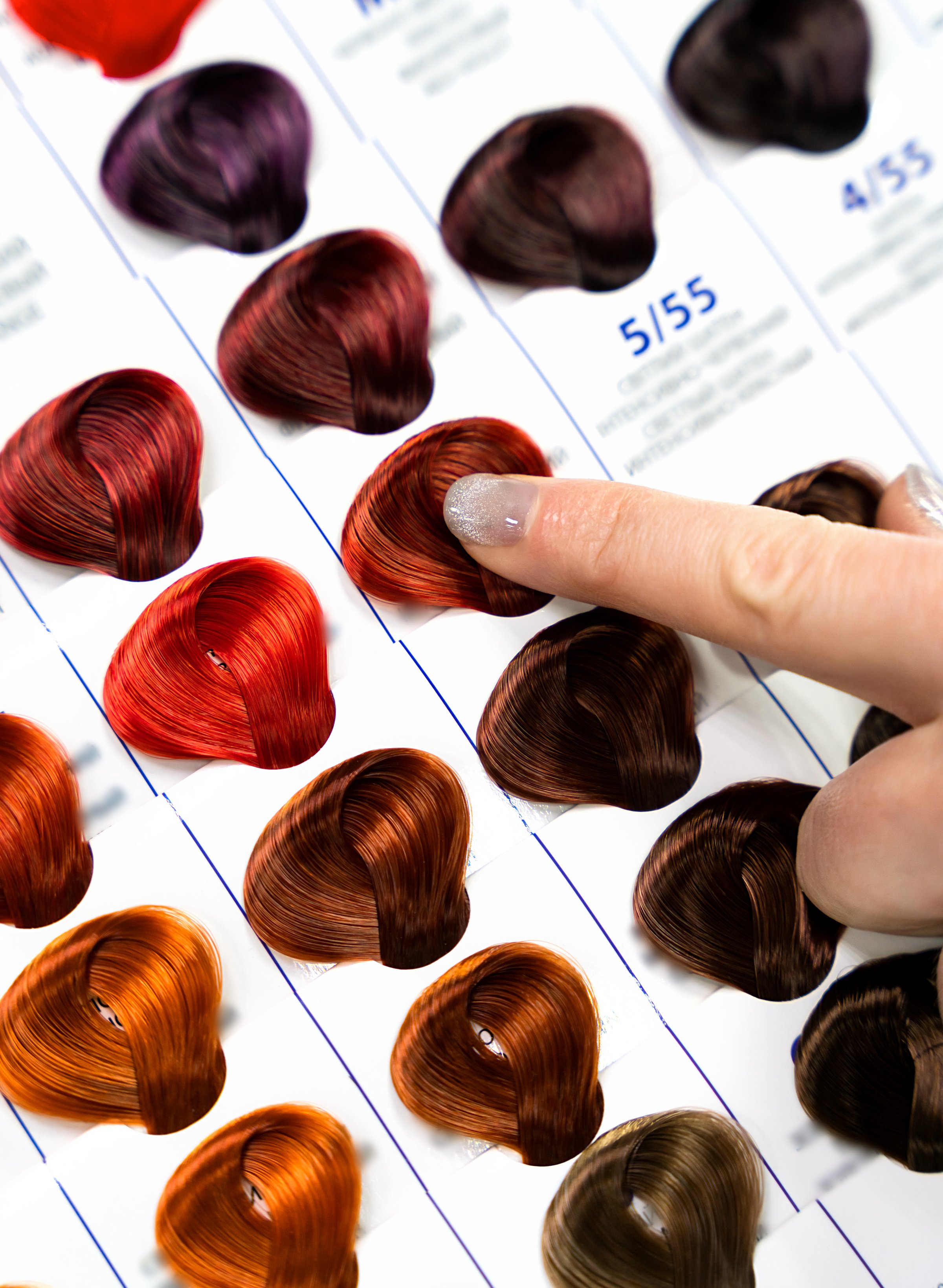A woman points to a hair color on a palette with hair dye samples. Close-up. Selective focus.