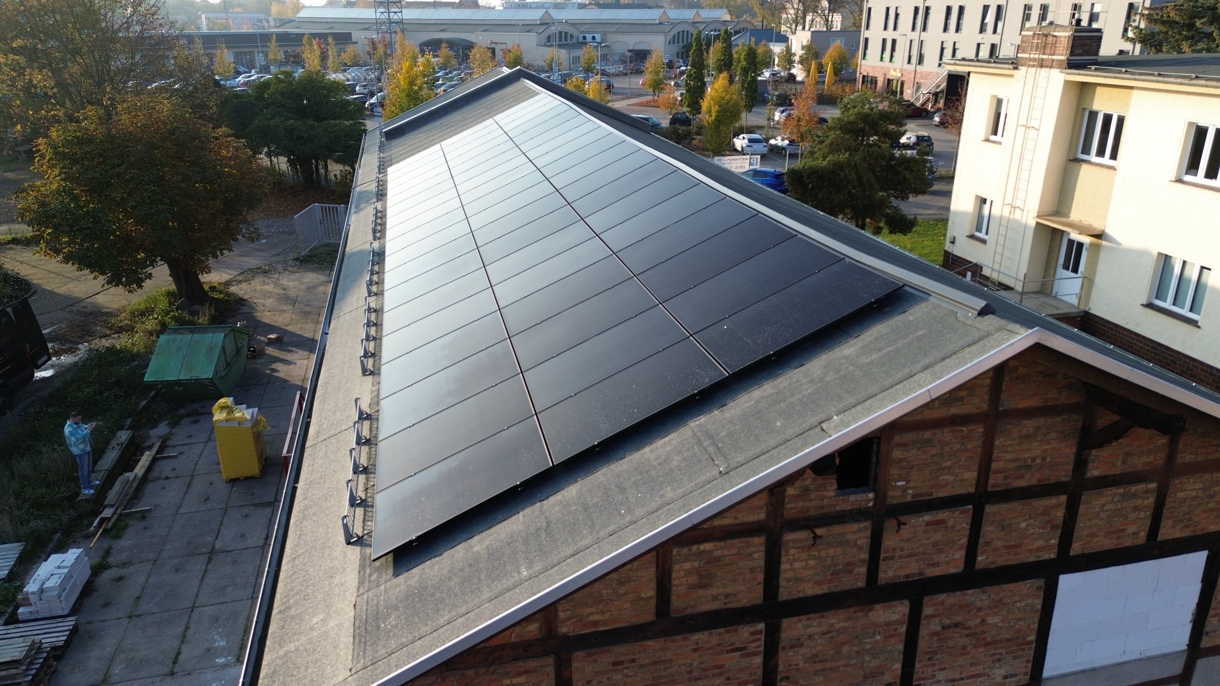 Solar panels installed on the roof of a brick building, surrounded by trees and adjacent constructions.