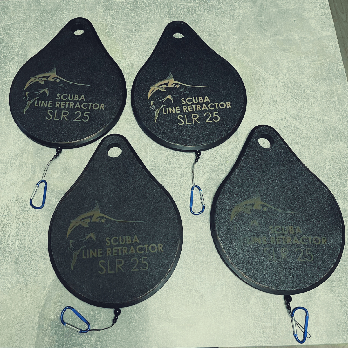 Four scuba line retractors labeled SLR 25, each with a clip, arranged on a gray surface.