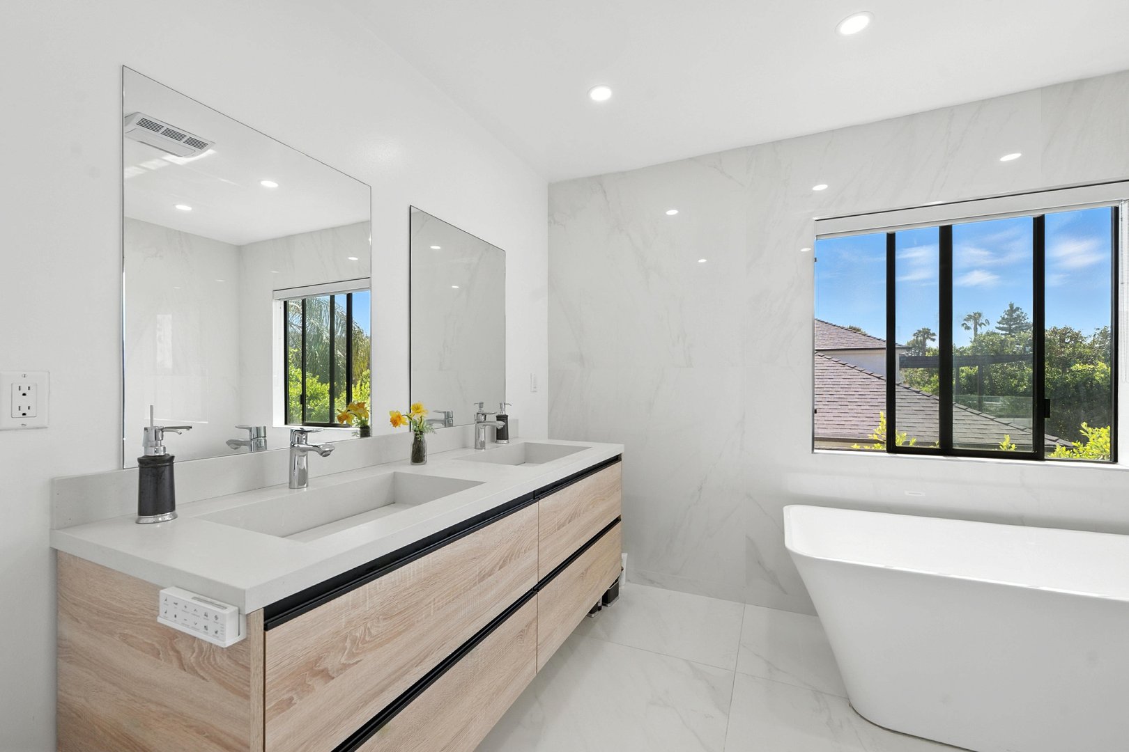 Modern bathroom with a freestanding tub, double vanity, large mirror, and marble-look walls and floor.