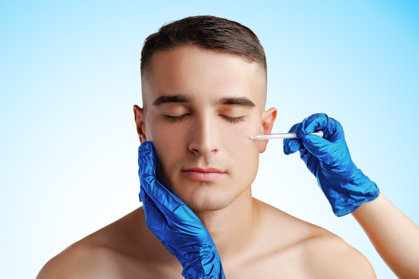 Handsome young man face and beautician hands with syringe making cosmetic injection in face studio shot