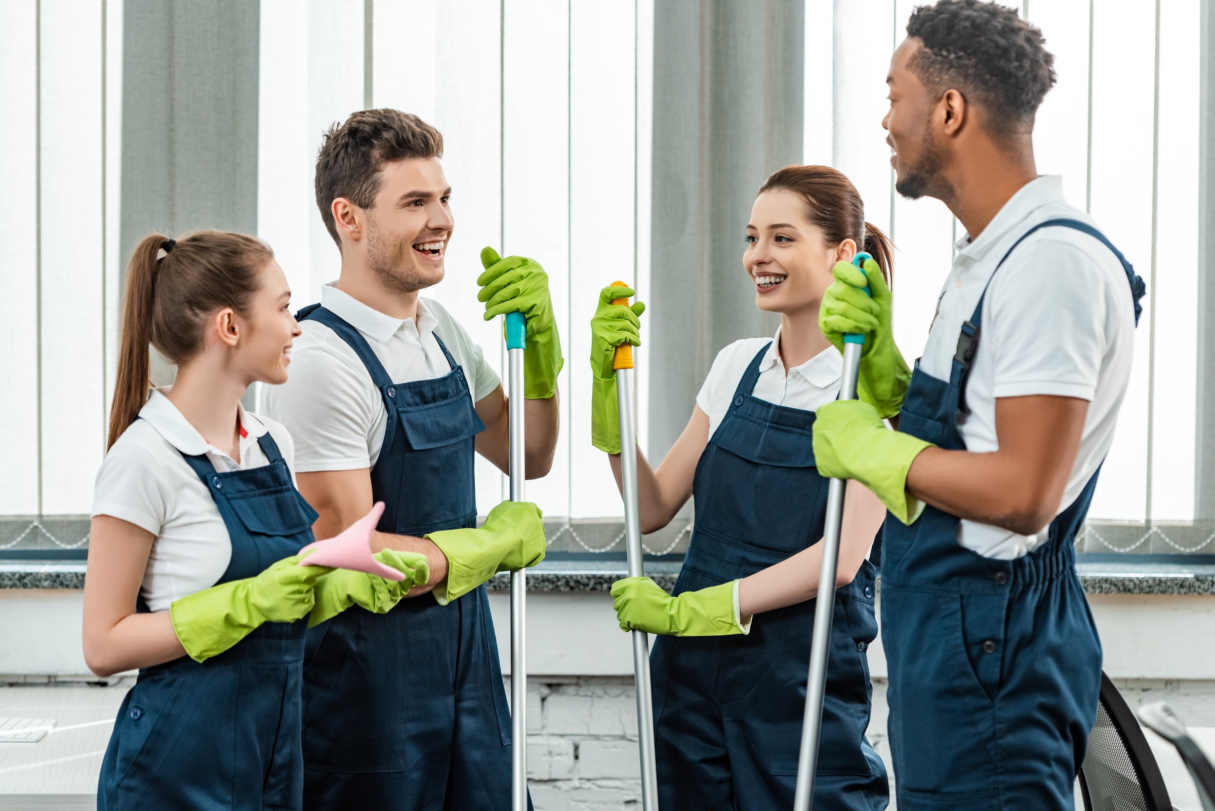 smiling multicultural team of cleaners talking while standing in office