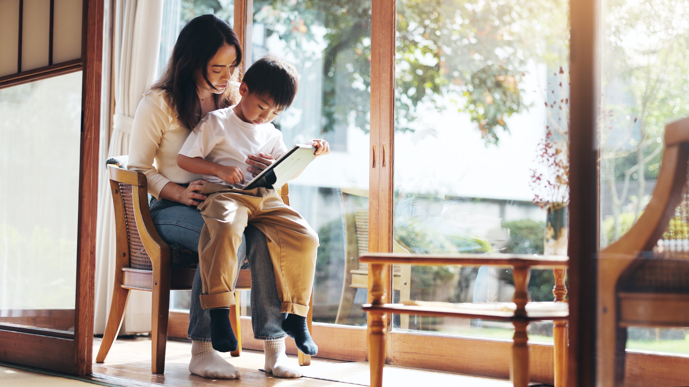 Reading, study or tablet with mother and son on chair in home for child development or learning. Education, Japanese family or technology with single parent woman and boy in apartment for search