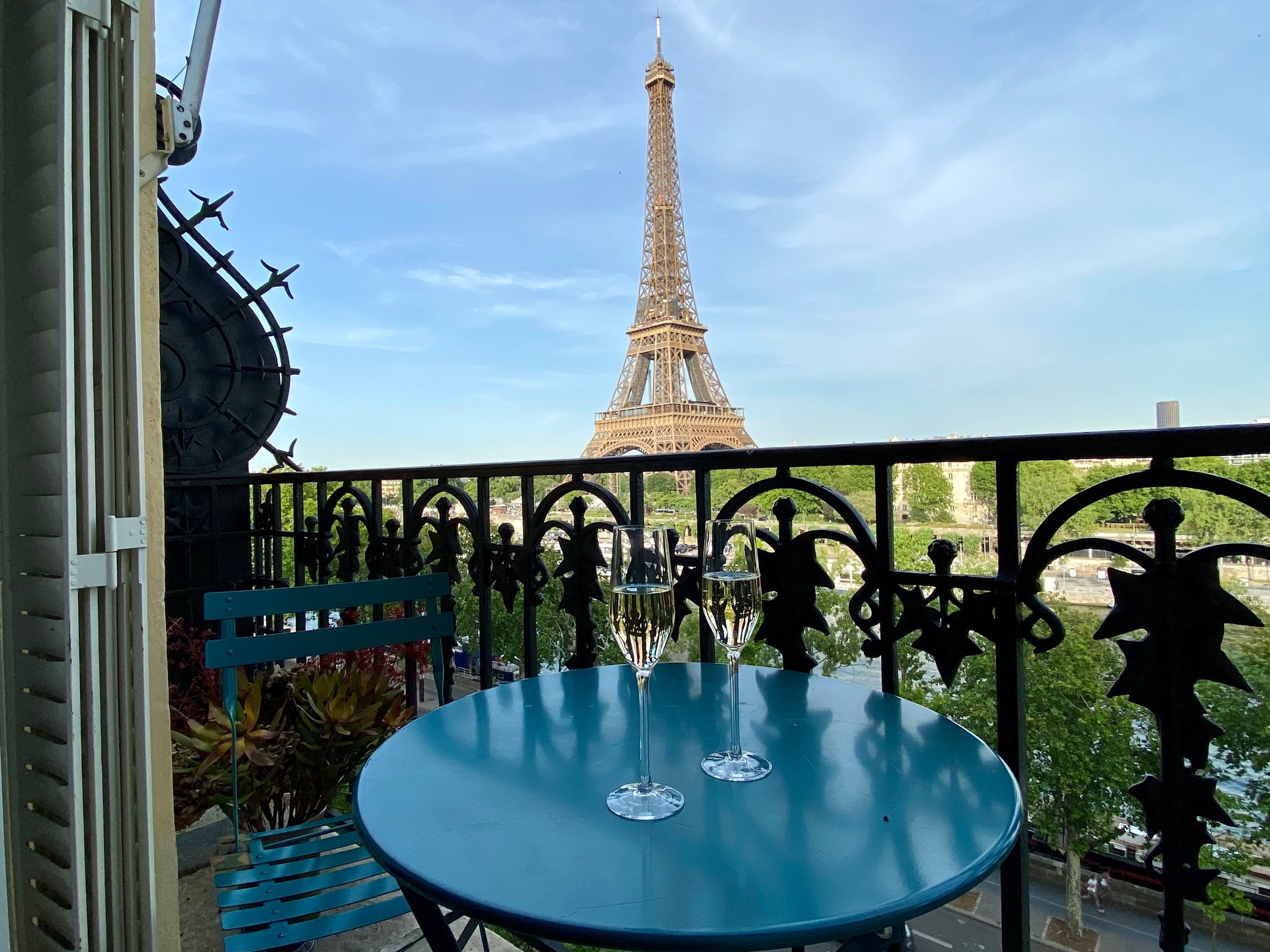 View of the Eiffel Tower from an apartment balcony with two champagne glasses on a small metal table