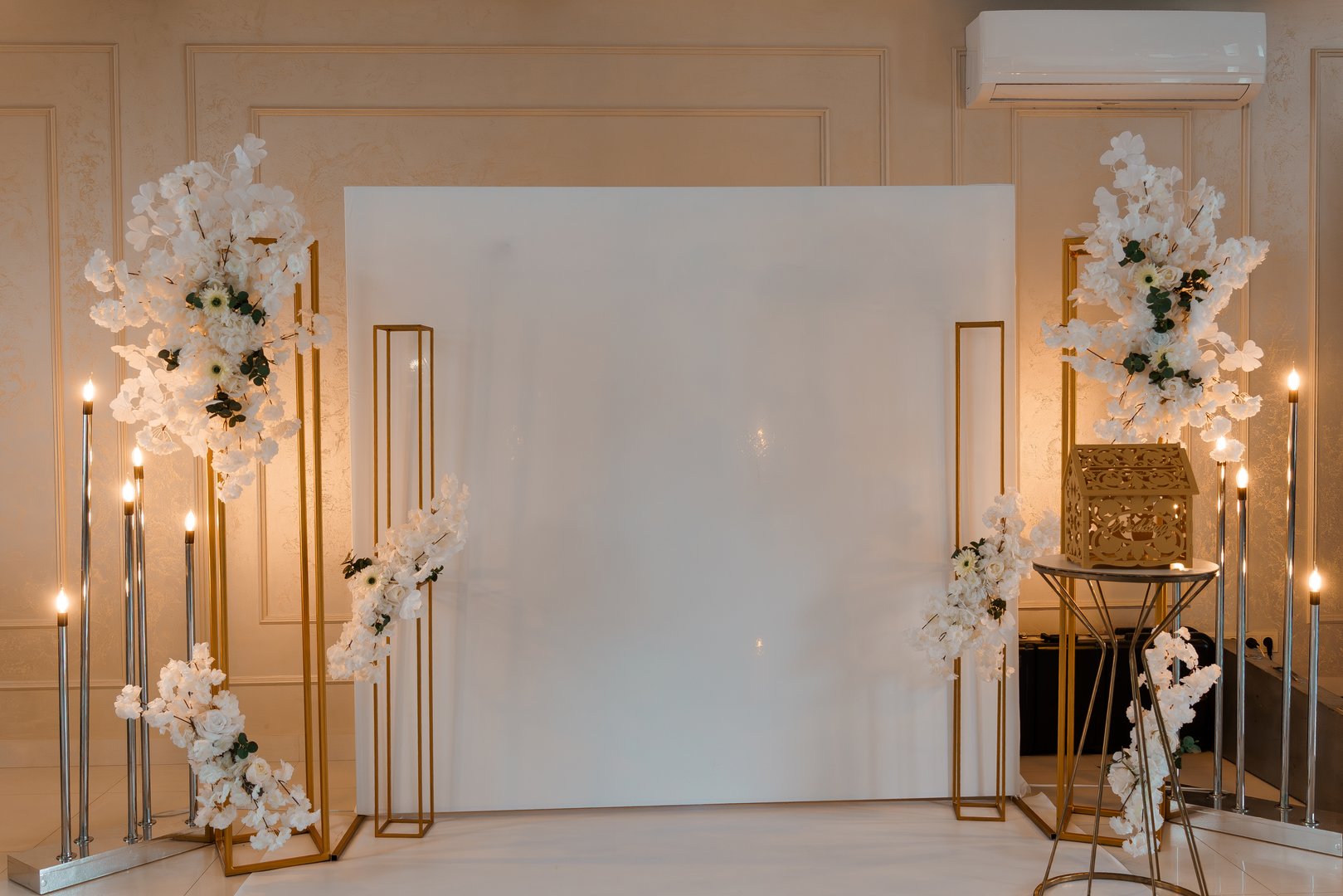 Luxurious wedding stage decoration featuring white flowers, gold metal frames, candles, and a blank canvas backdrop ideal for photoshoots and ceremony use
