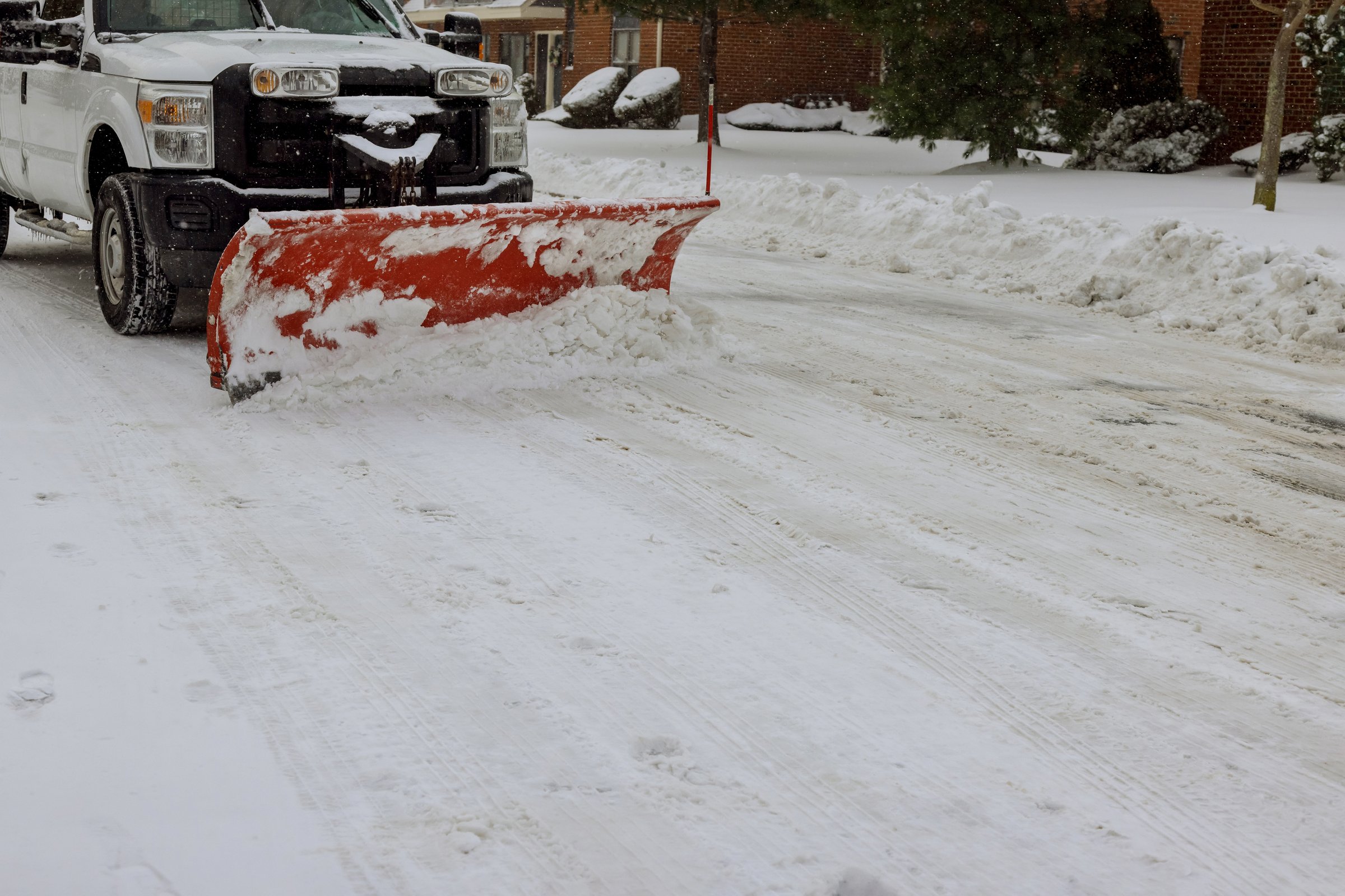 Snow plow clearing snowy residential street in Eagle River, highlighting winter maintenance and snow removal services.