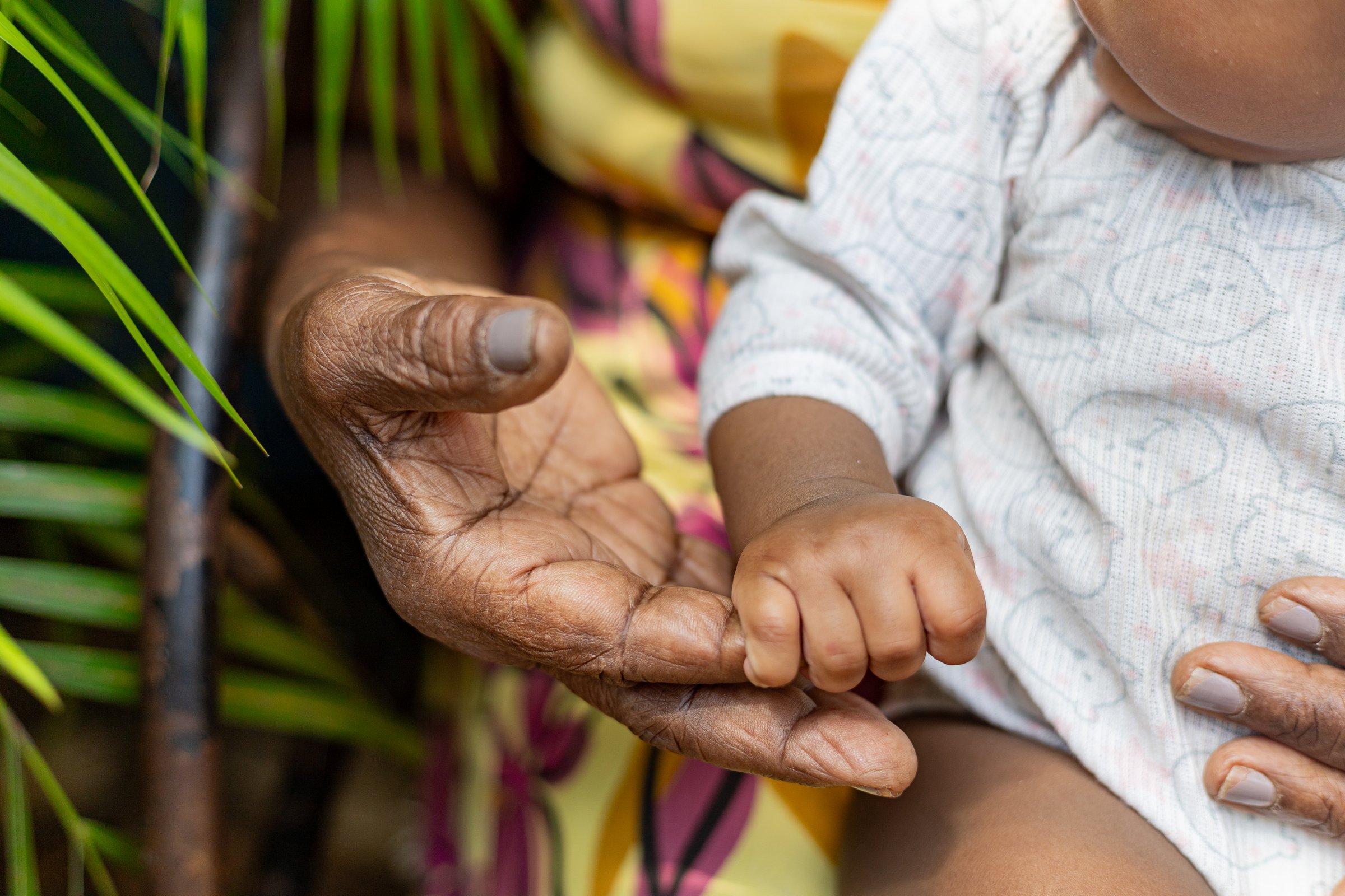 Grandmother sitting in her rocking chair with her great granddaughter with plants in the background. African woman