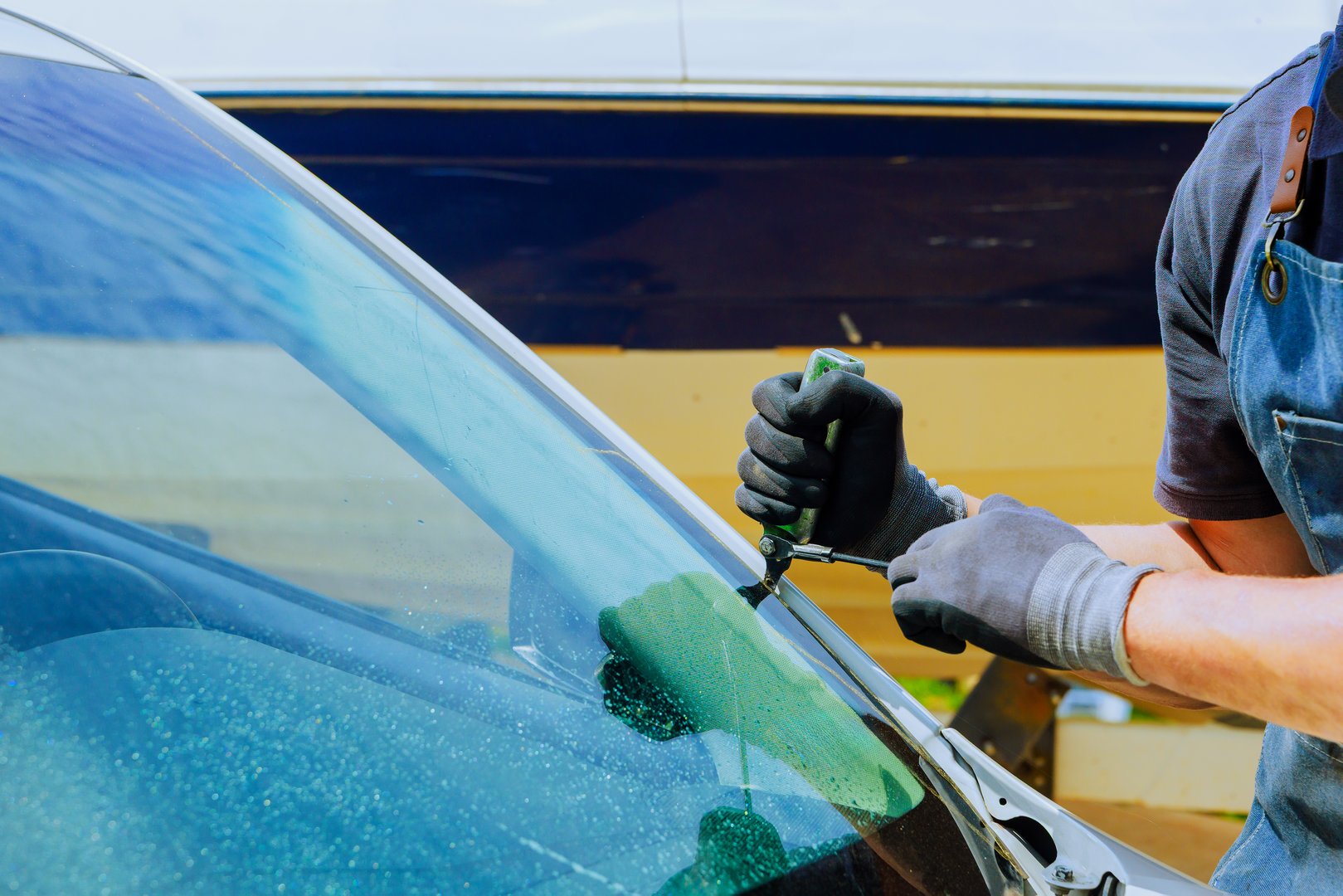 Technician replaces damaged windshield using special tools with precision while working at an auto service center.