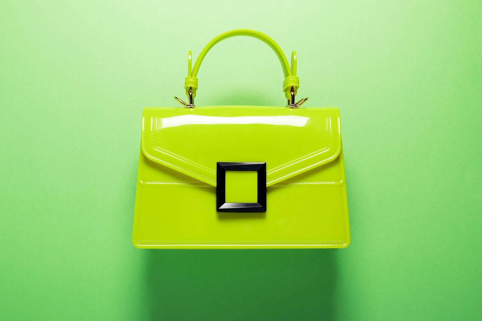 A green vinyl handbag flat lay against a matching green background, creating a monochrome composition with a modern, minimalistic aesthetic