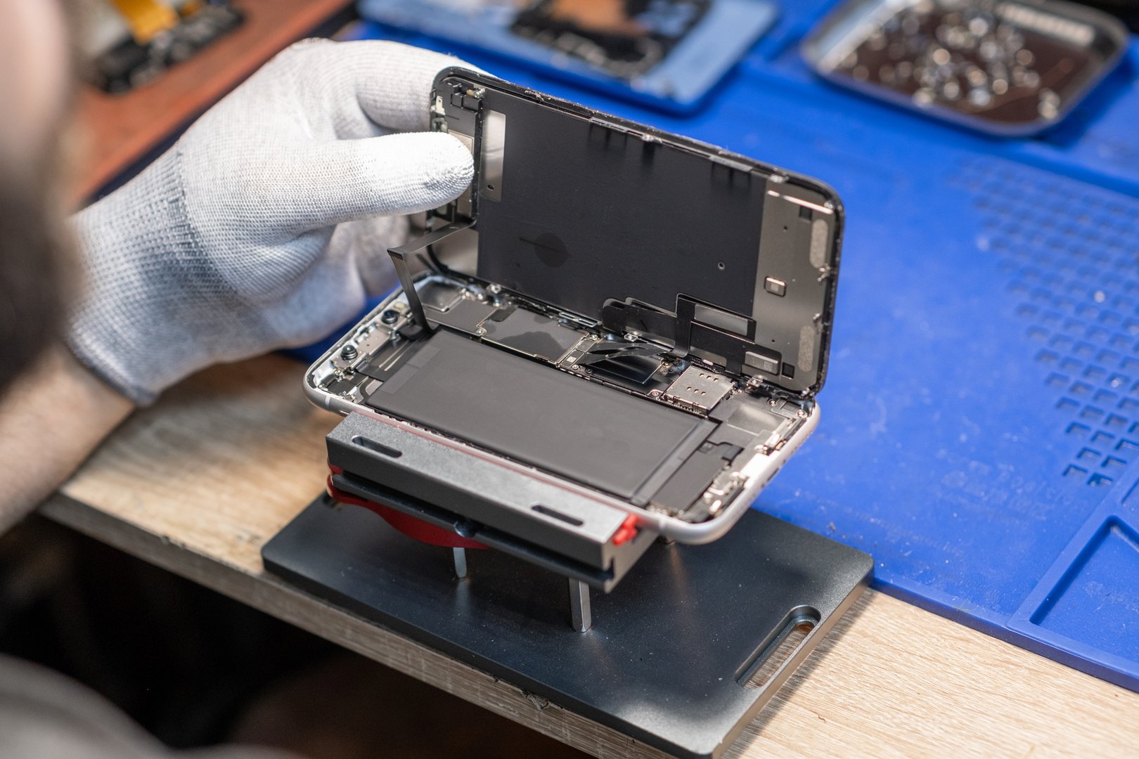 A technician carefully replaces a smartphone battery while working in a well-equipped tech repair workshop.