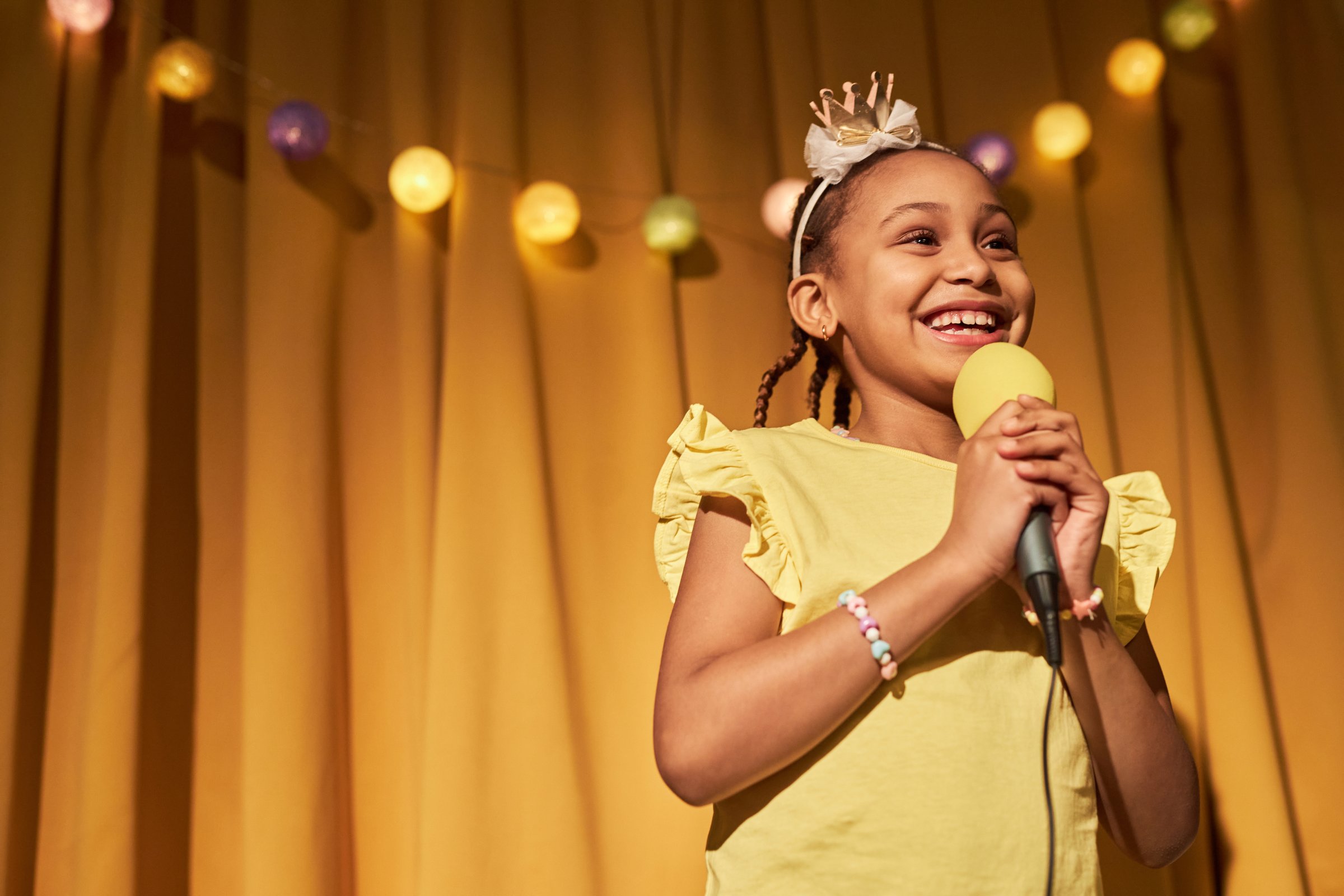Waist up portrait of smiling Black girl speaking to microphone while giving home concert and show performance copy space