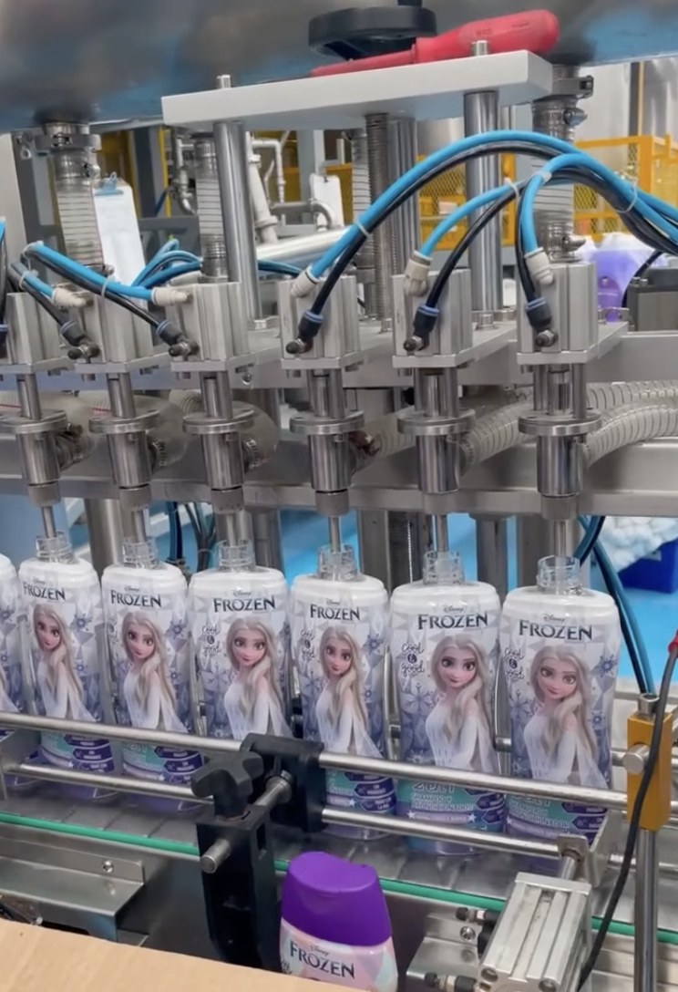 Factory machine filling "Frozen" themed juice cartons with tubes in a production line.