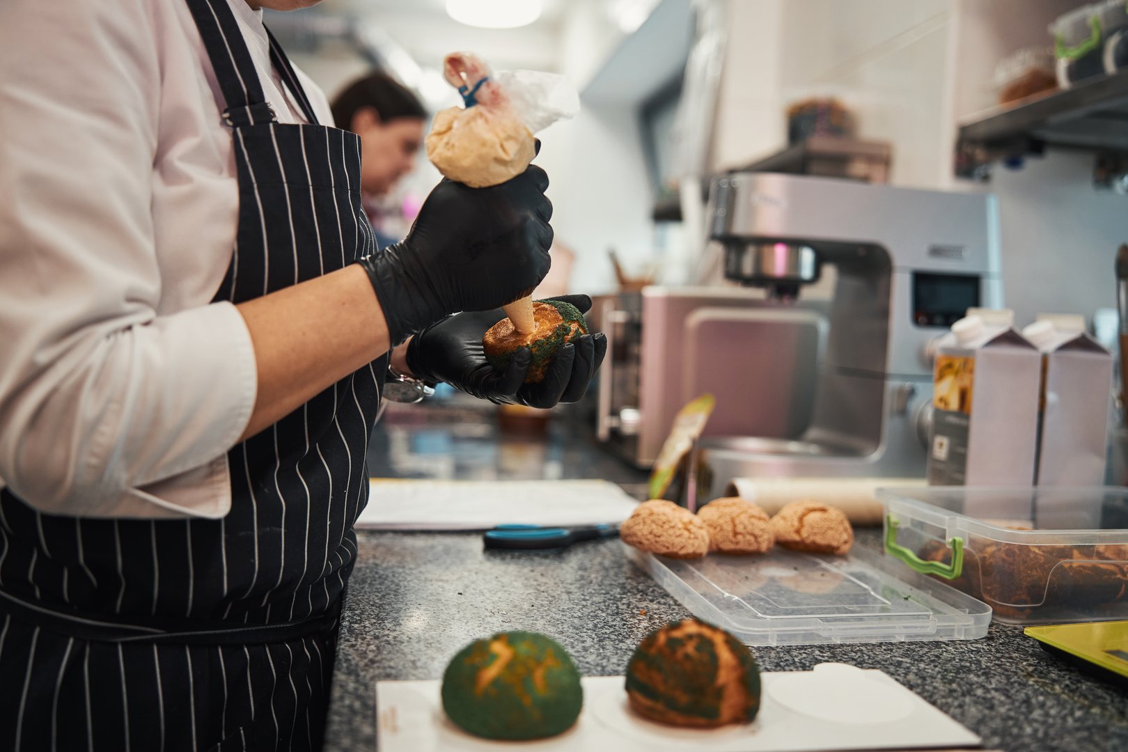 Chef decorando panecillos con guantes de nitrilo negros en cocina profesional.