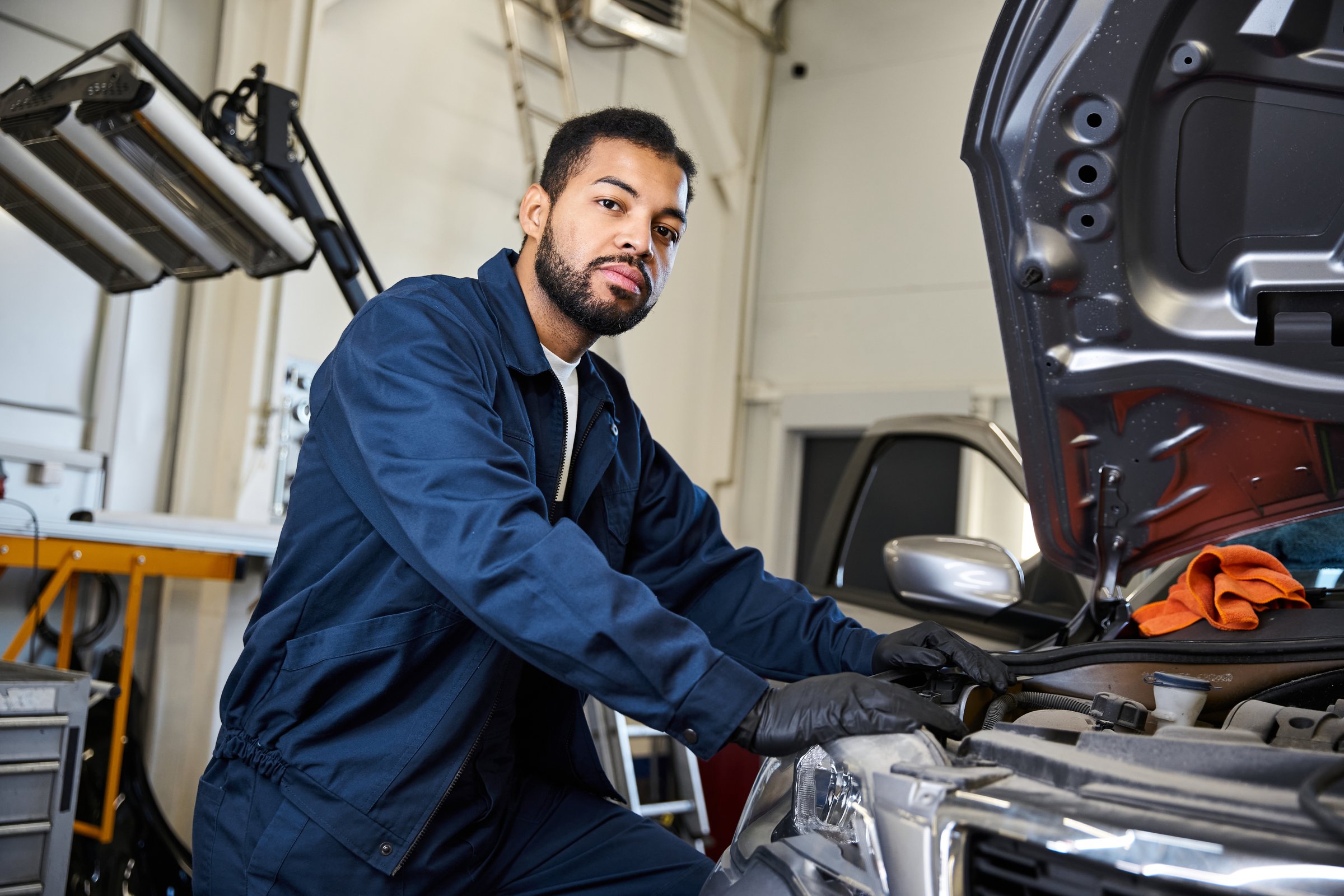 A skilled young mechanic performs car maintenance in a busy auto service center.