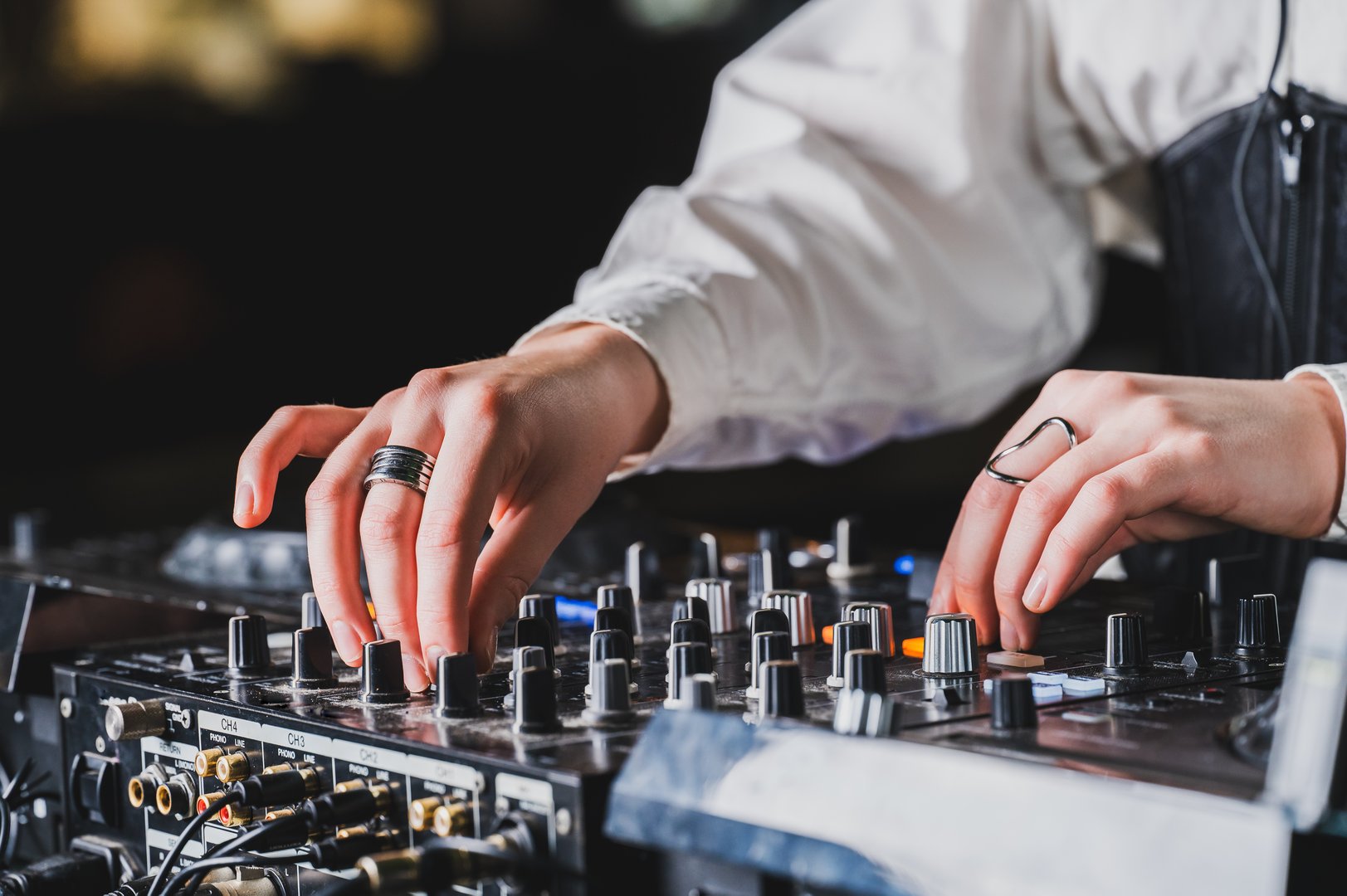 Close-up of a DJ's hands adjusting knobs on a professional mixer, creating music in a dark club. The vibrant atmosphere is captured with a shallow depth of field