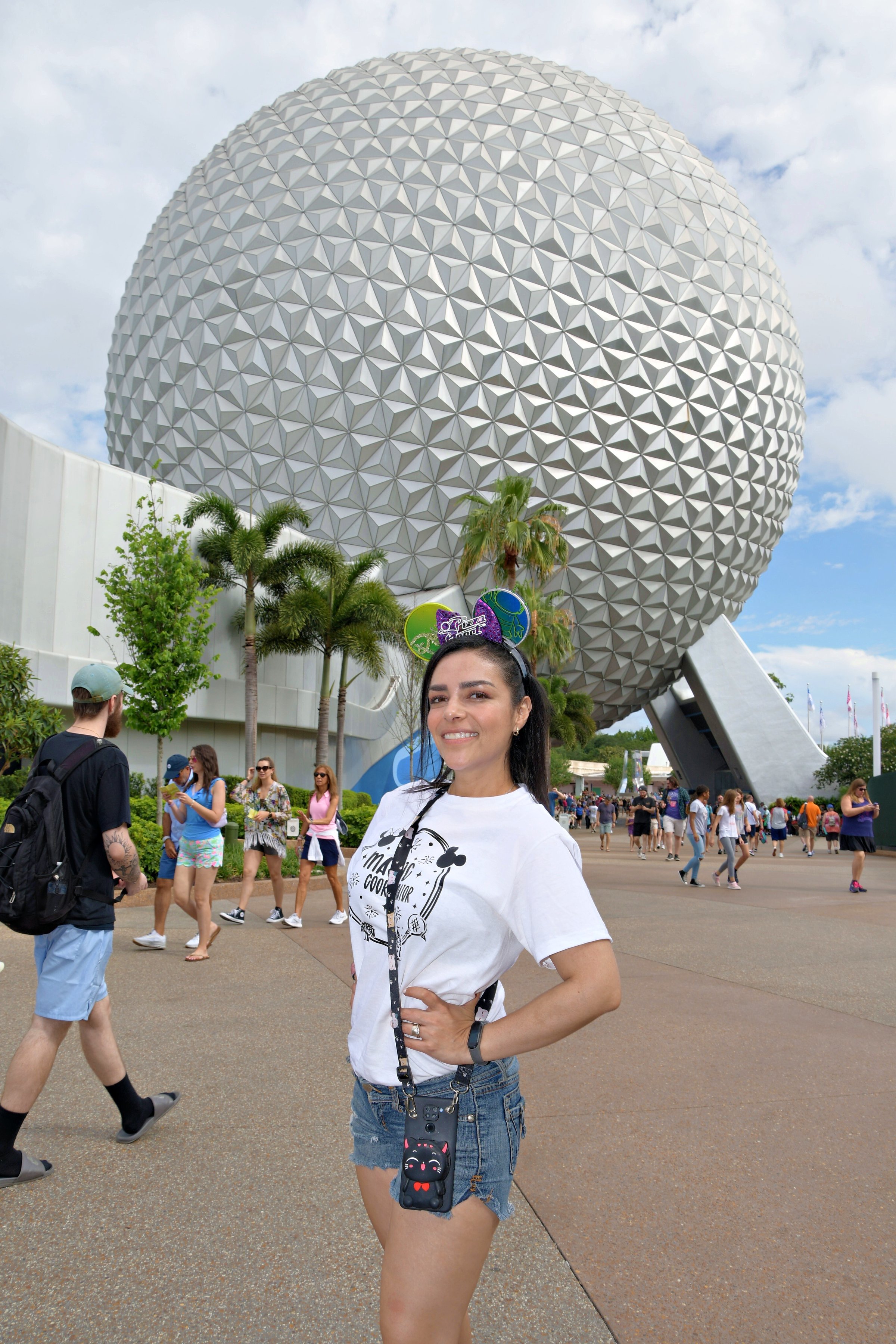 Woman posing in front of Epcot's Spaceship Earth at Disney World, wearing Mickey ears and a white t-shirt.