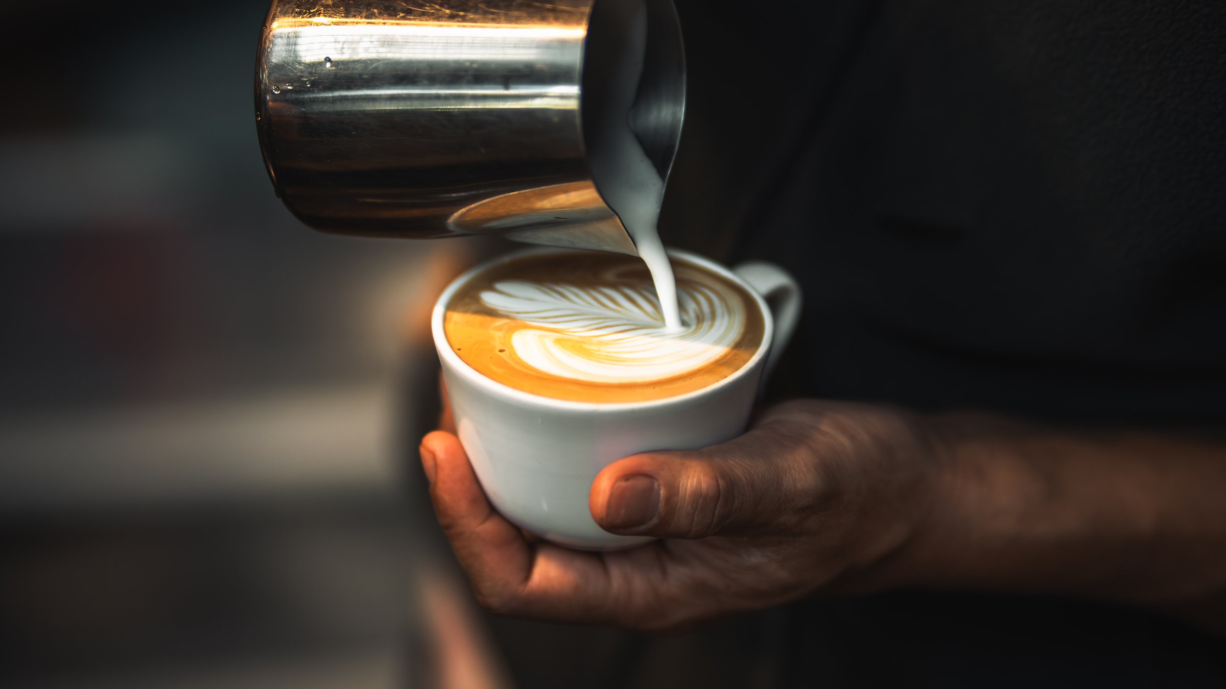 barista hand pouring milk for making latte art in cafe