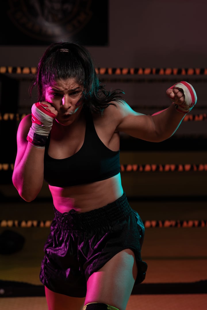female Latina boxer with her hands bandaged working out at a training session at a gym throwing a punch and looking at the camera with a serious determined expression.