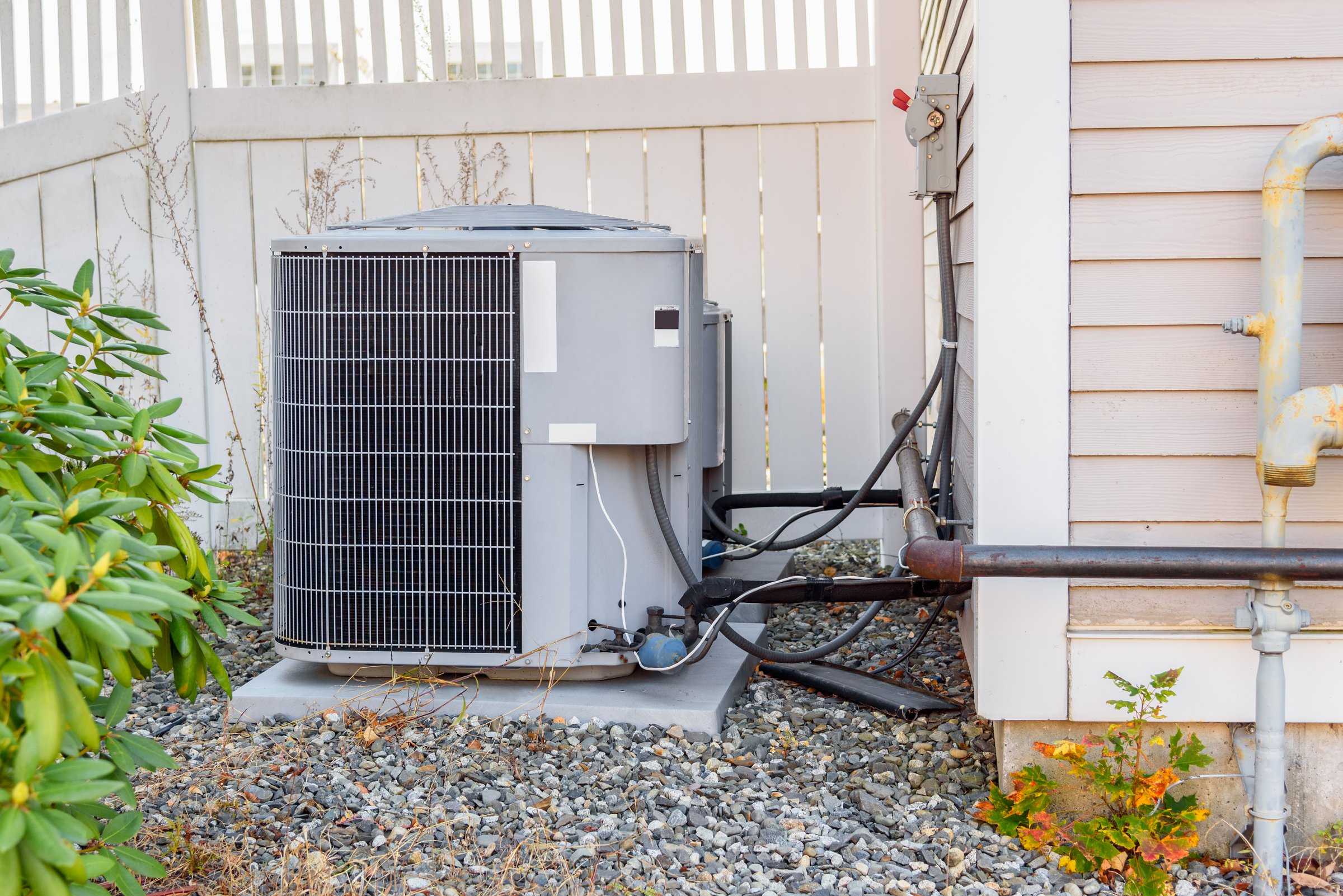 HVAC system external unit by a wooden fence in a house backyard. Bath, ME, USA.