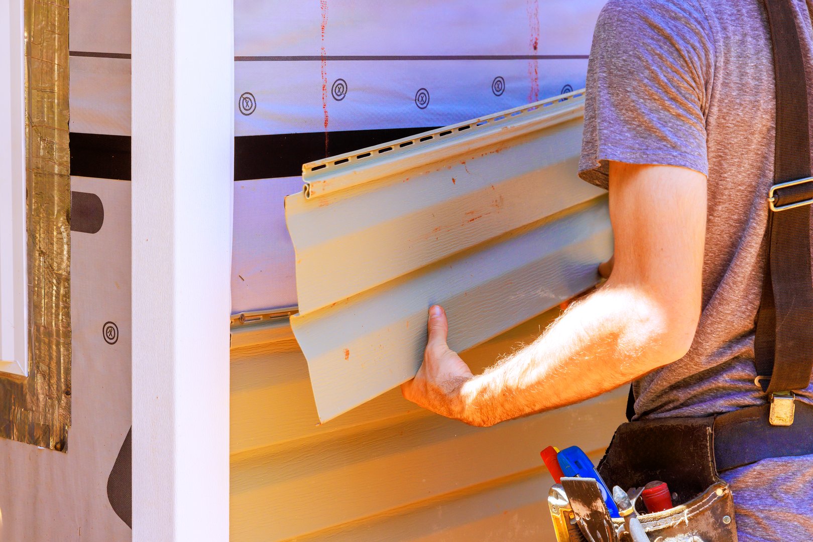 Construction worker carefully fits PVC siding panels into house, ensuring proper alignment