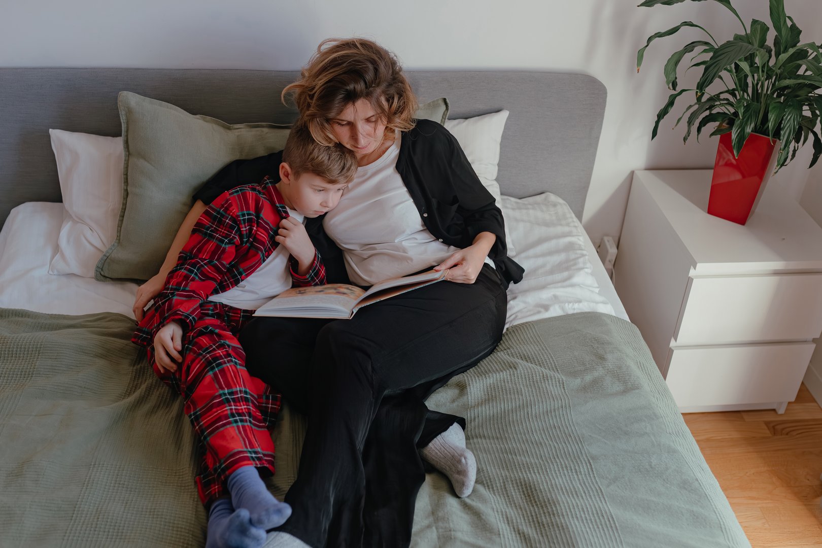 Mother holding child close while both observe storybook during calm daylight