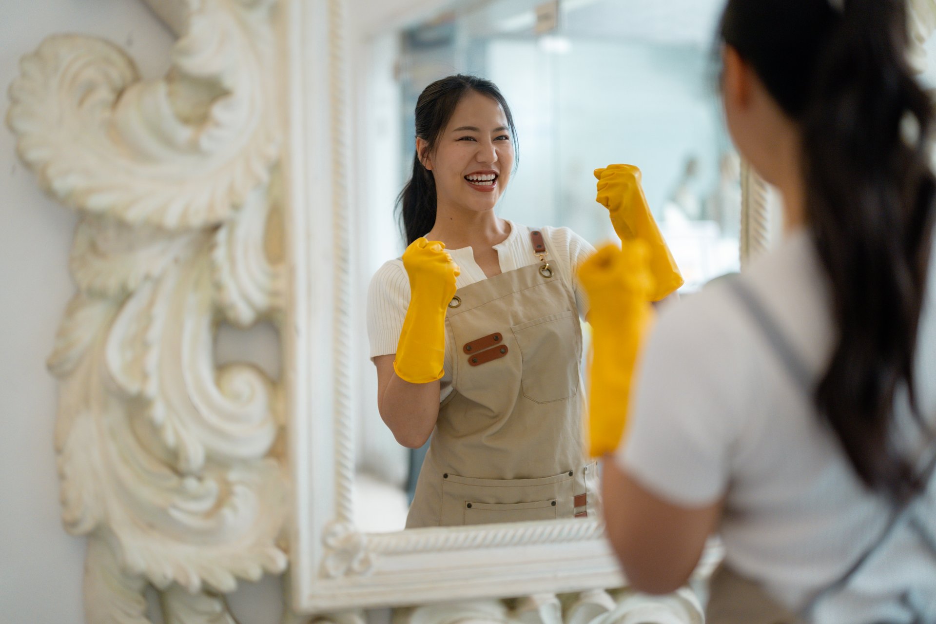 Cheerful cleaning professional in bright yellow protective gear celebrating success while checking reflection in mirror