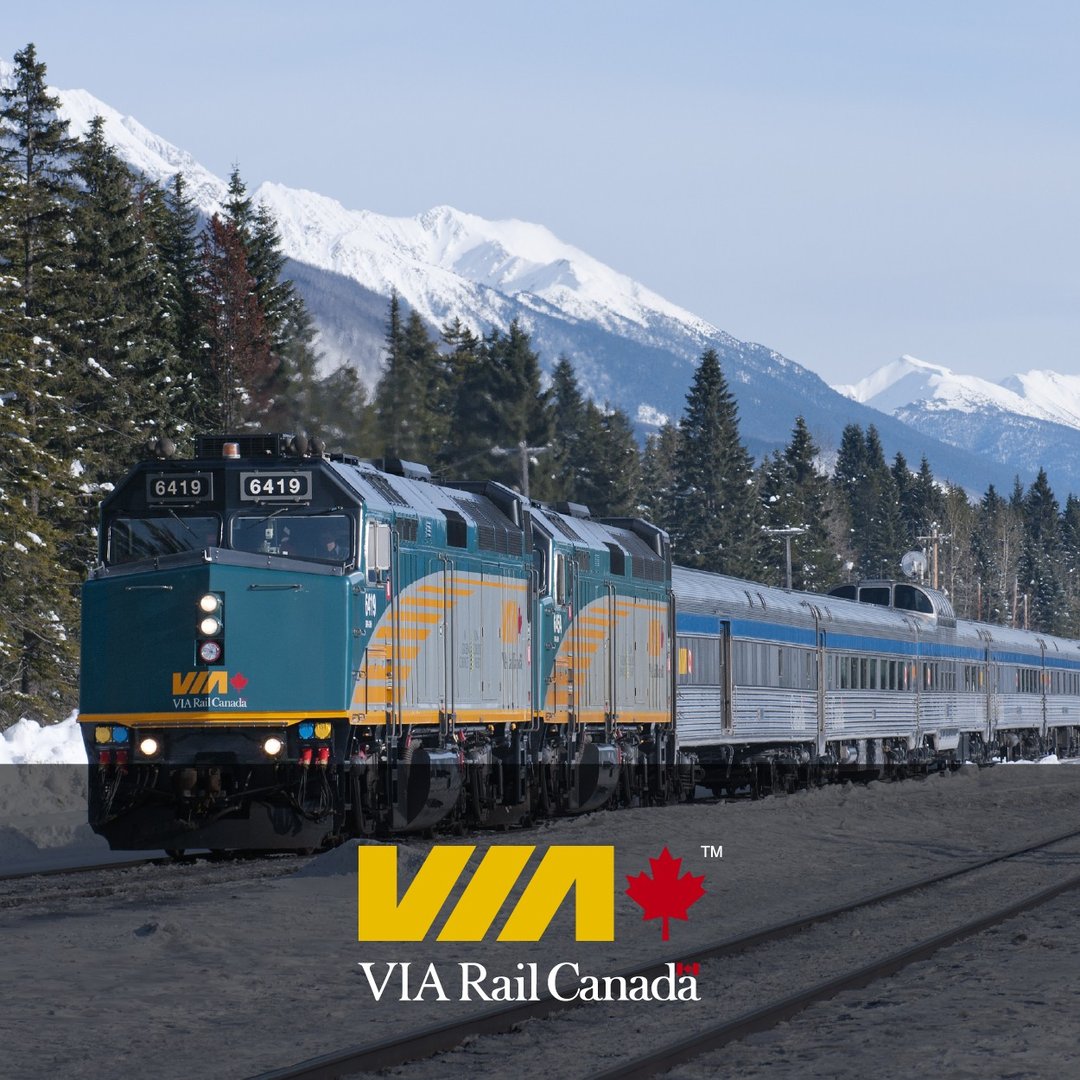 VIA Rail Canada train traveling through snowy mountain landscape with trees and clear skies.