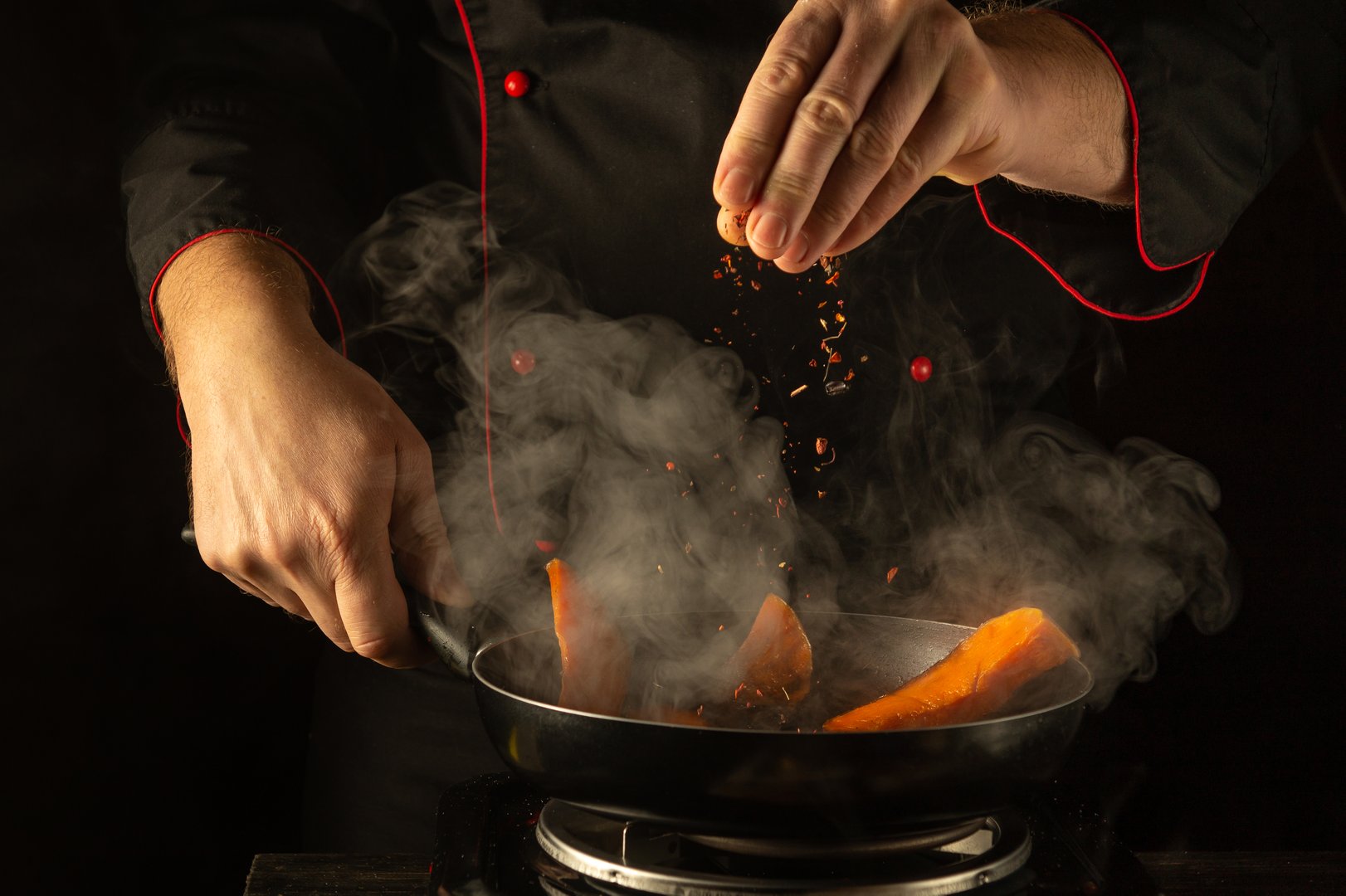 In a warm kitchen, skilled hands sprinkle aromatic spices into a pan of brightly colored vegetables. The rising steam and rich colors create a tantalizing atmosphere of culinary creativity.