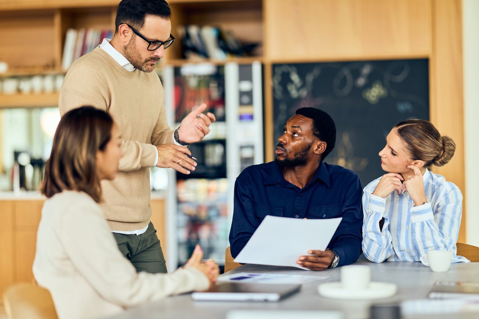 Team members listen as a presenter explains ideas using a document in a bright workspace.