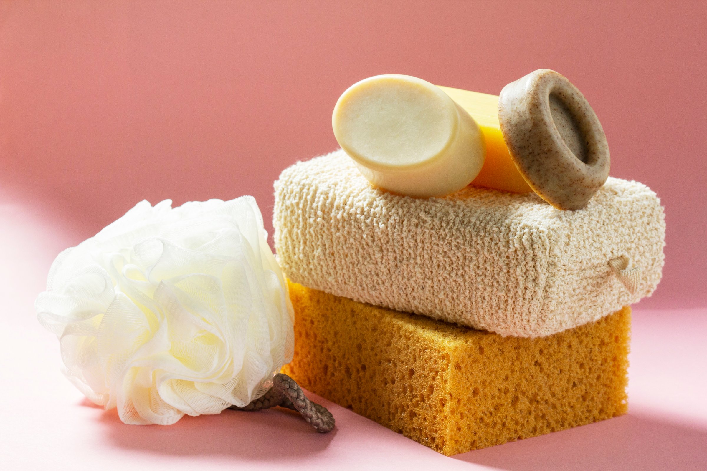 Set of bath accessories, sponges of different sizes and shapes and handmade soap on a pink background. Individual set for body skin care.