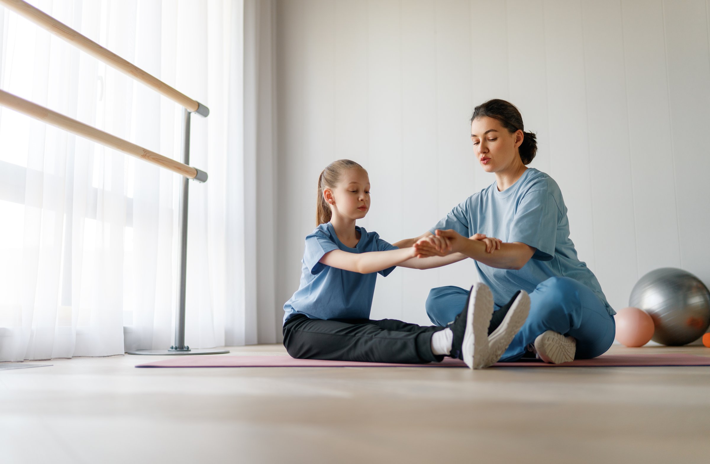 The child is undergoing physical therapy. The girl is doing exercises under the doctor's supervision.