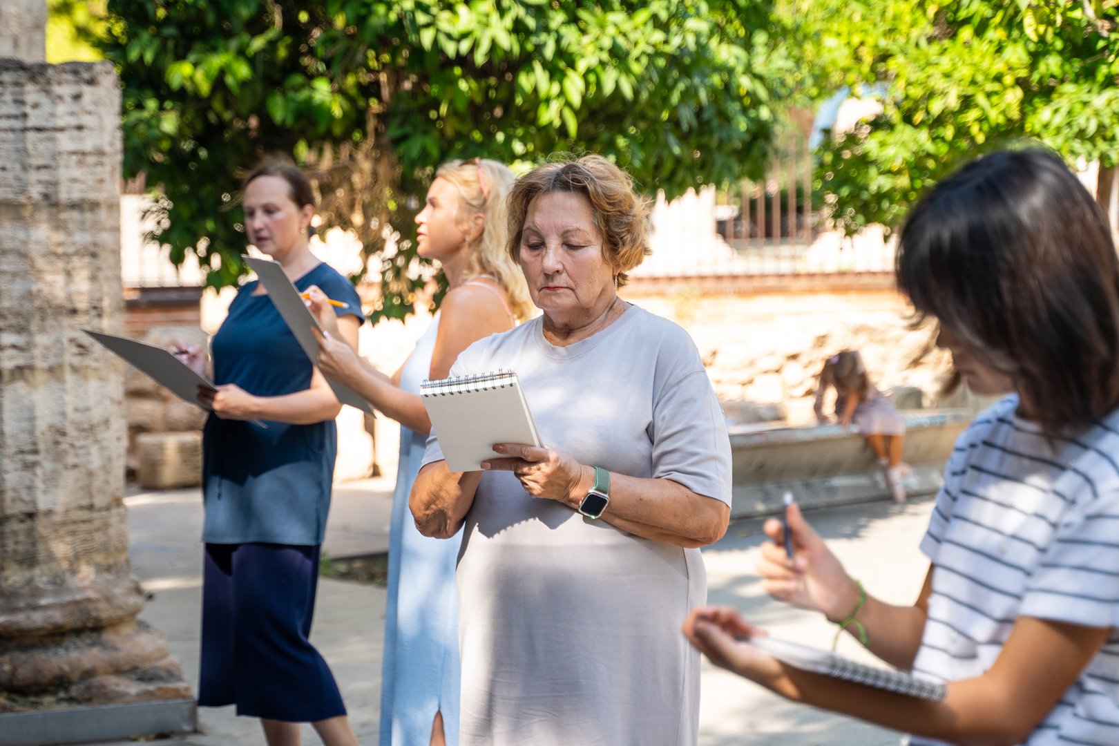 Art outdoor plein-air workshop. Group of artists Senior Woman, teenager girl draw with pencil sketch. Skeleton drawing architecture. Educational art creative concept