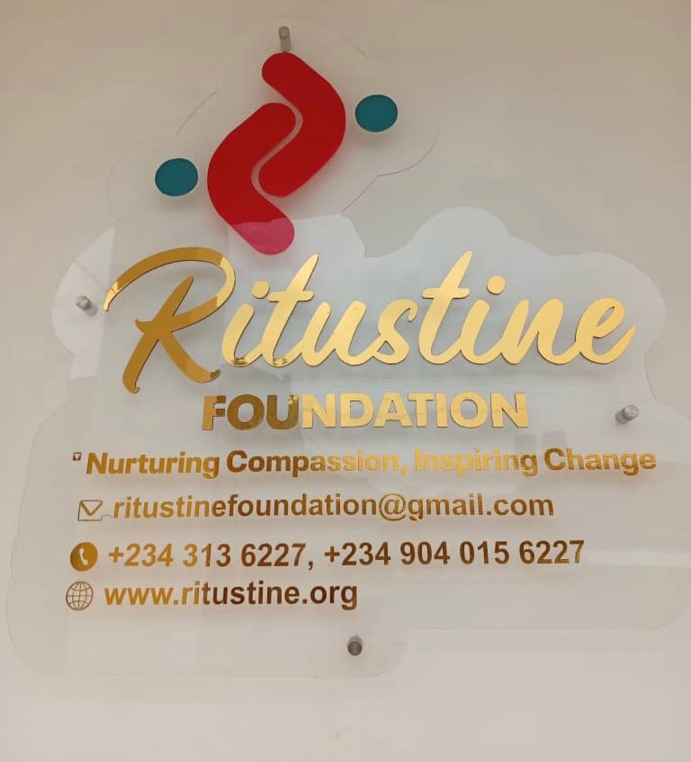 Ritustine Foundation sign with logo, contact email, phone numbers, and website URL on transparent background.
