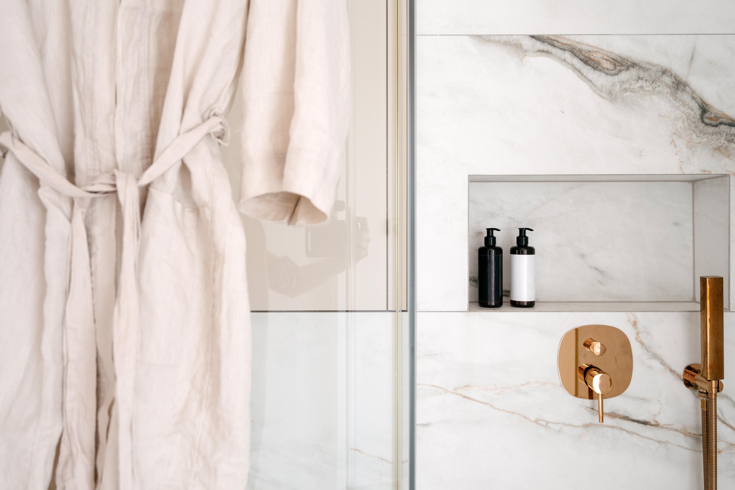 Close up shot of bathrobe in hotel bathroom features sleek marble walls and a luxurious shower area. A relaxing robe hangs nearby, accentuating the sophisticated design of the residential space
