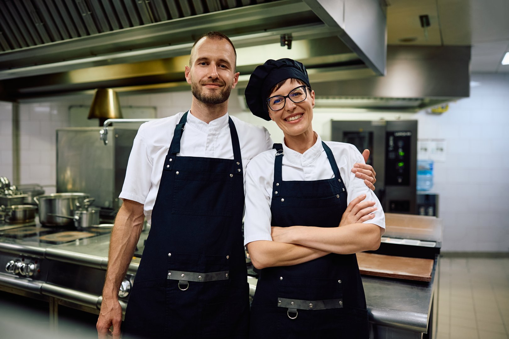 Happy professional cooks working in a restaurant and looking at camera.