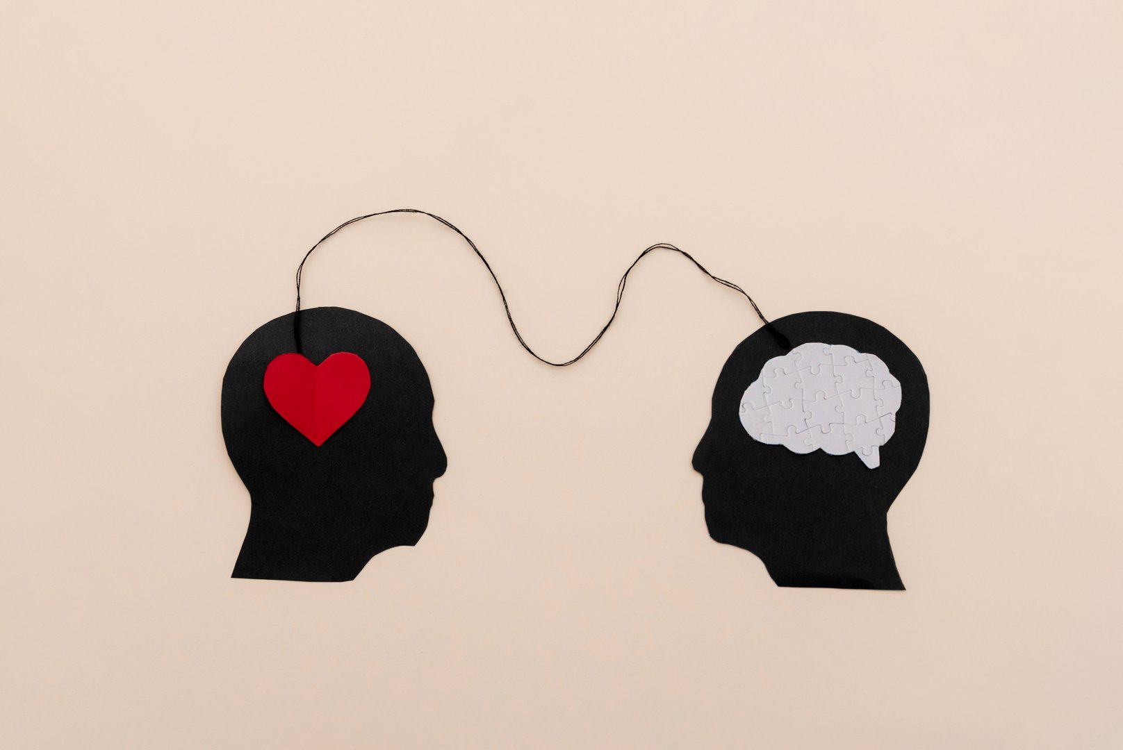 Silhouettes of two black human heads connected by a string symbolizing emotional intelligence and logical connection