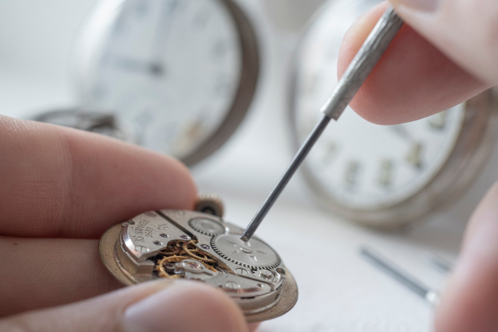 Professional watchmaker repairer working on an old vintage pocket watch in a workshop.