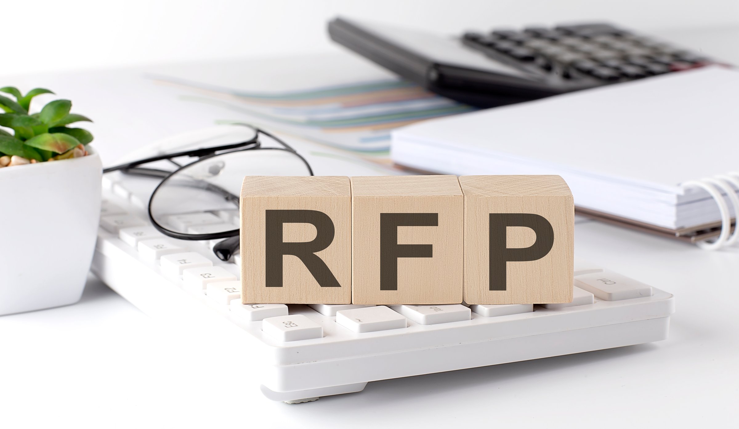 RFP written on wooden cube on keyboard with office tools