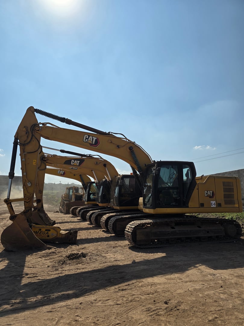 A row of parked yellow Caterpillar excavators at a construction site under a clear blue sky.