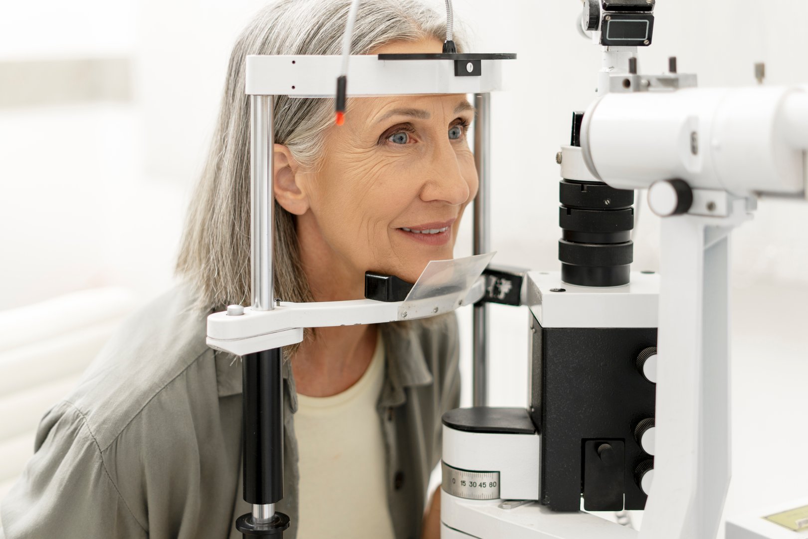 Smiling senior woman undergoing an eye exam using a phoropter in a modern ophthalmology clinic, demonstrating the importance of regular eye checkups for maintaining good vision and eye health