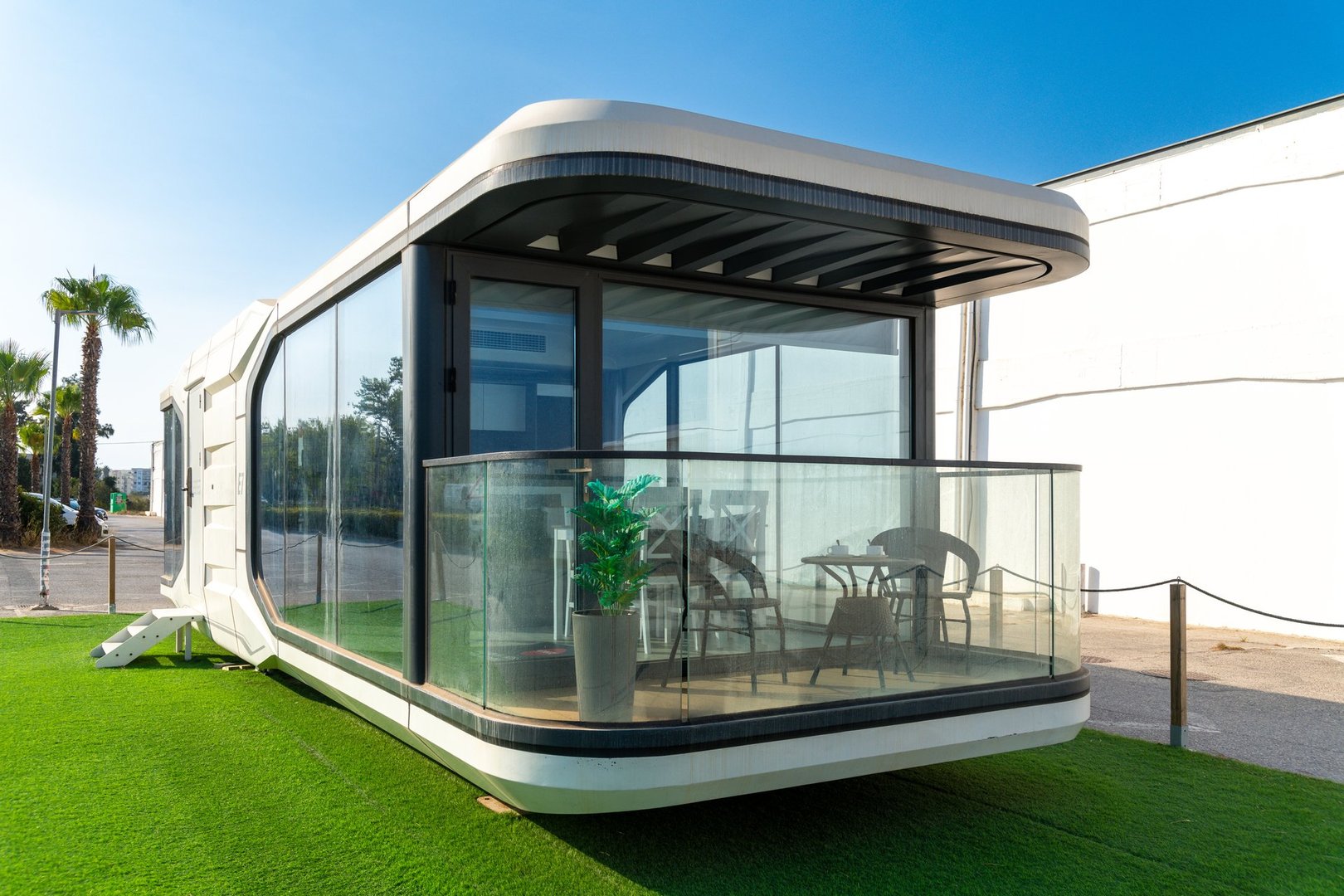 Almancil, Algarve - Portugal - 09-19-2024: Modern modular building E7 with glass front, terrace with furniture, and a green environment under a clear blue sky.
