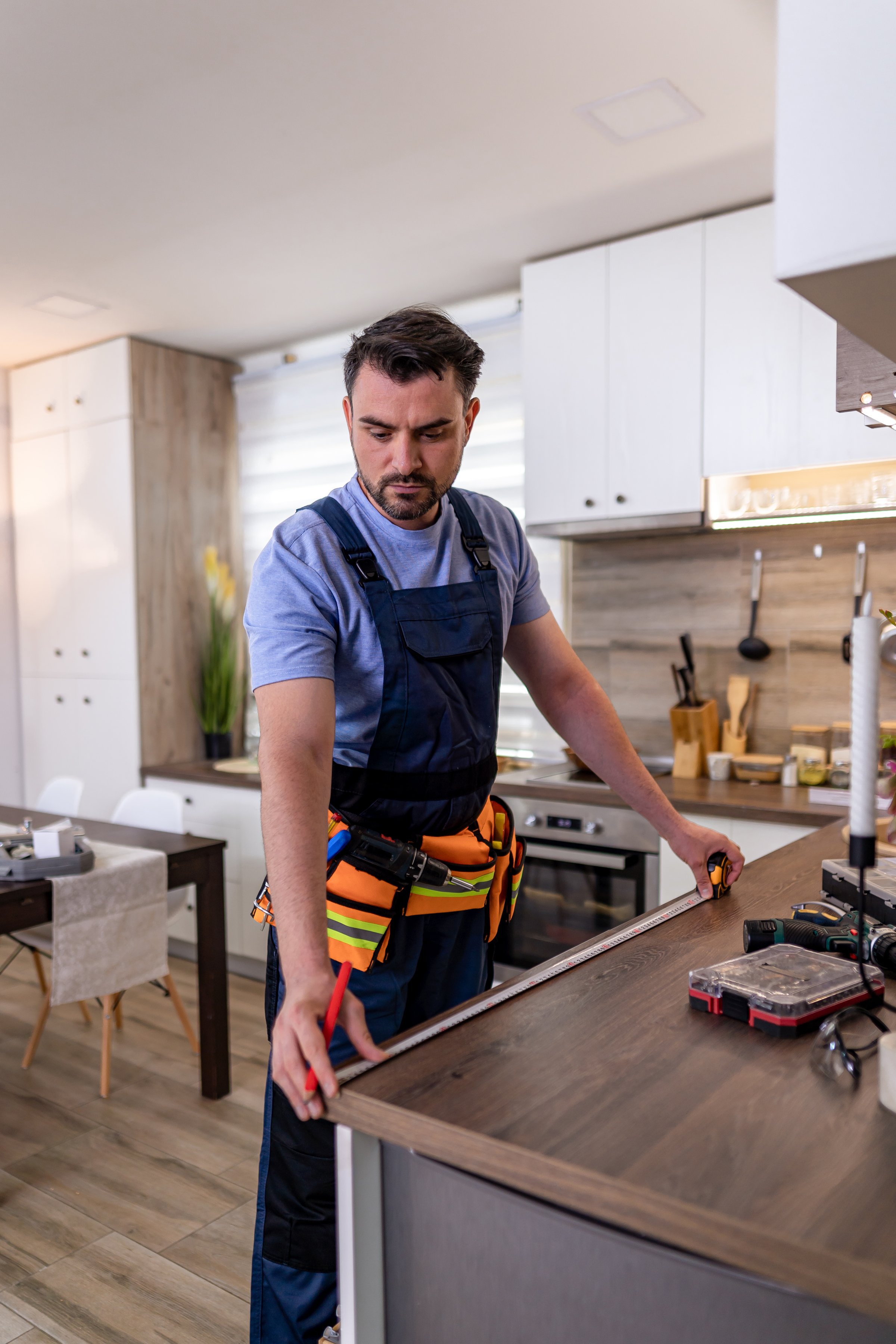 A professional is diligently measuring and fitting cabinetry in a contemporary kitchen.
