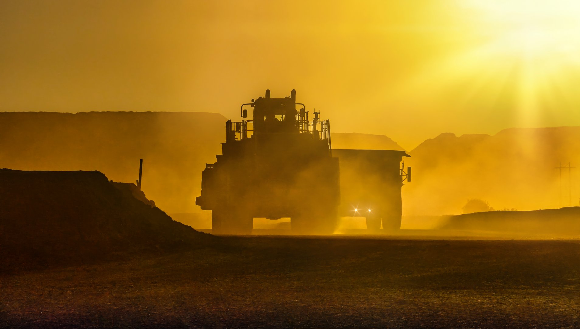 silhouette of truck mining equipment and front loader at a diamond mine ,outdoors sunset with orange sky and sun reflection rays late in the day