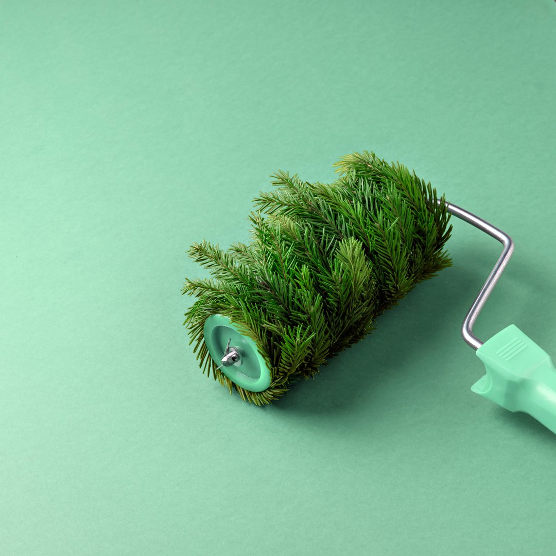 Paint roller covered with fir branches on a green background. A creative and unconventional concept combining nature and creativity, creating a fresh festive atmosphere.